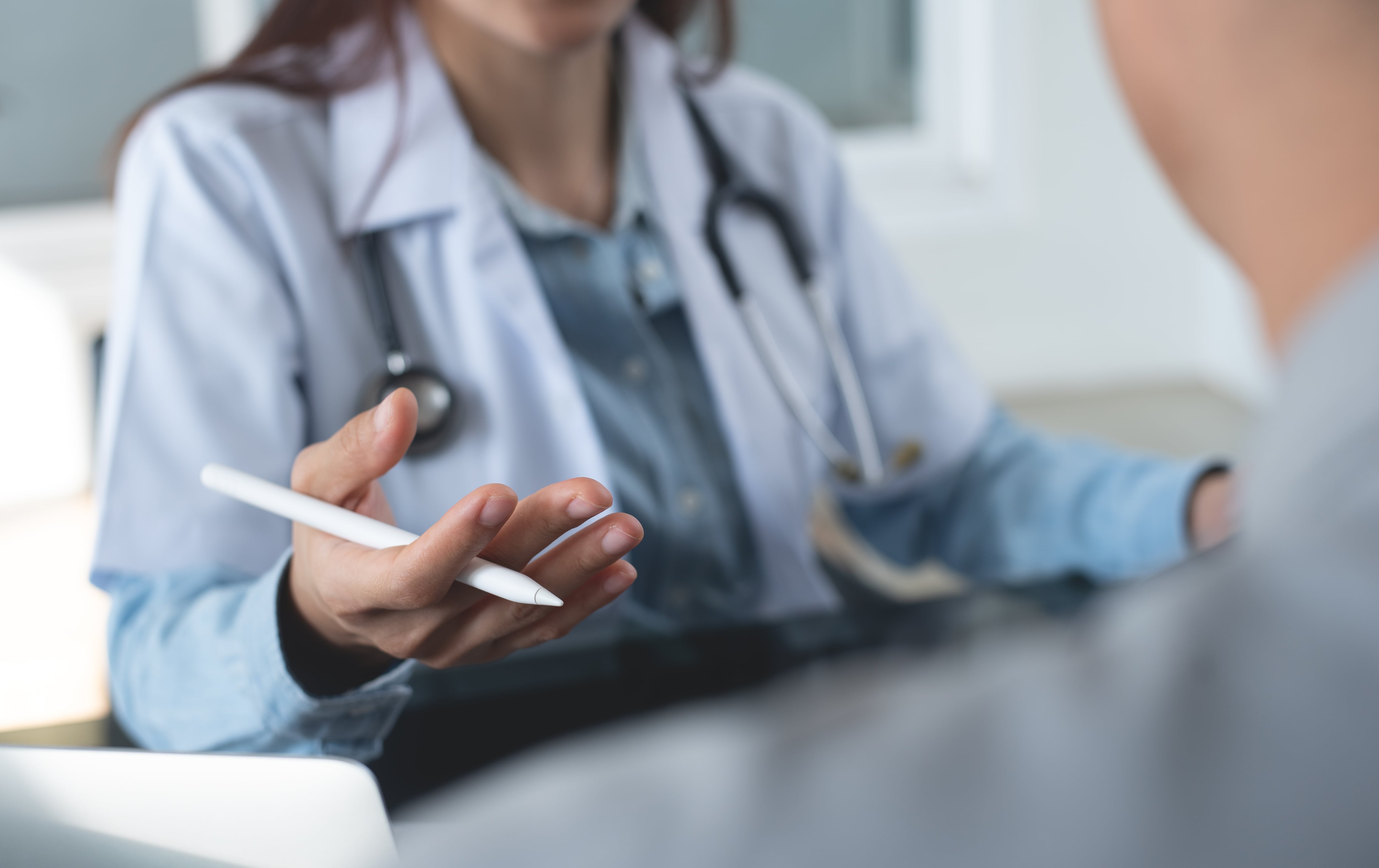 Primer plano con rostro no visible de médica con gabacha blanca y estetoscopio atendiendo a paciente
