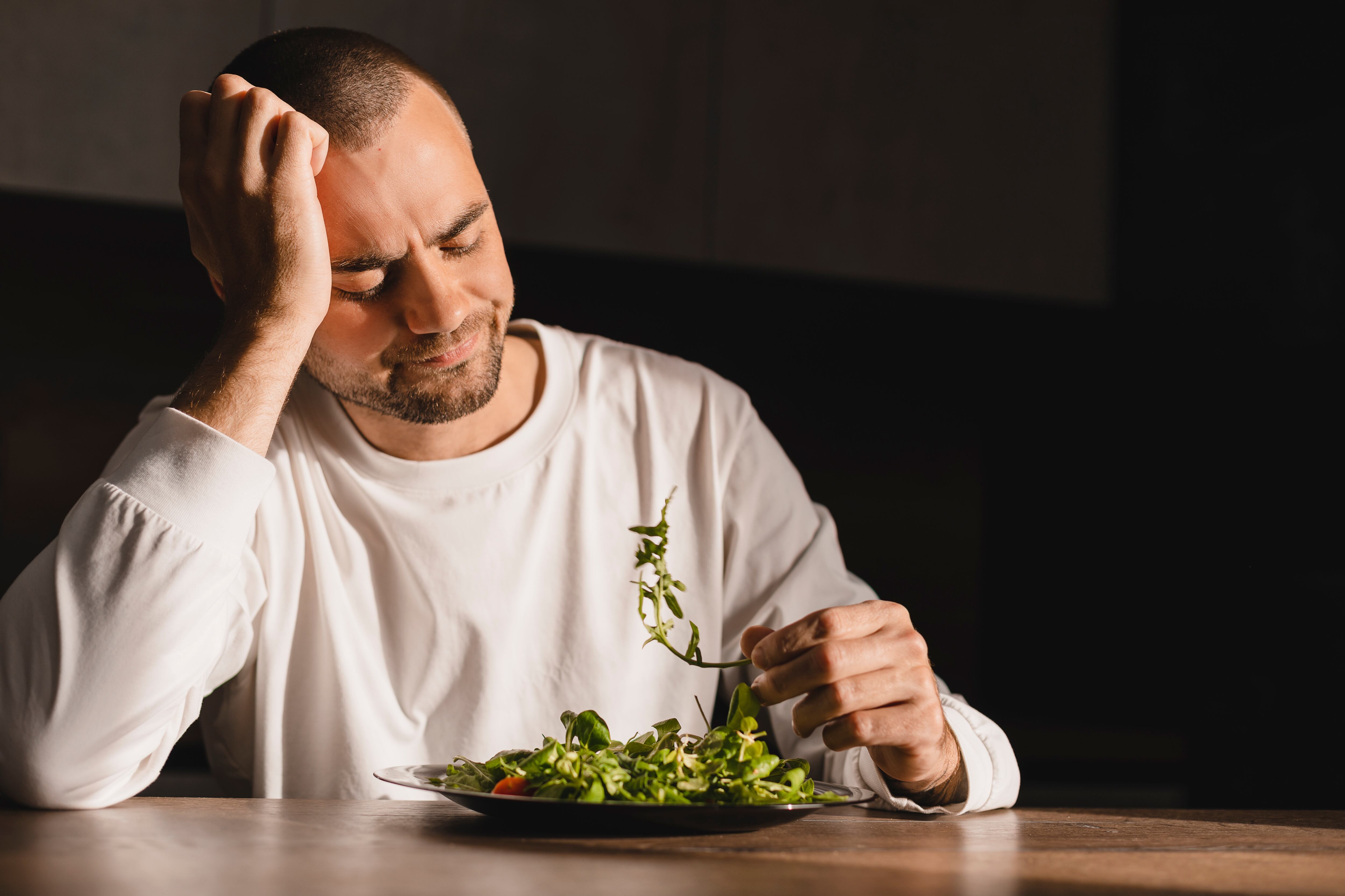 Un hombre comiendo una ensalada, pero no se ve contento con ella.