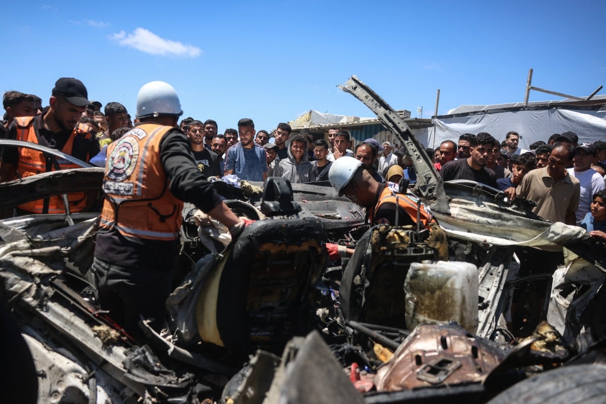 Miembros de la defensa civil palestina inspeccionan los restos de un vehículo alcanzado por un ataque israelí, mientras transeúntes observan la escena en Jan Yunis, en el sur de la Franja de Gaza, el 26 de mayo de 2026.