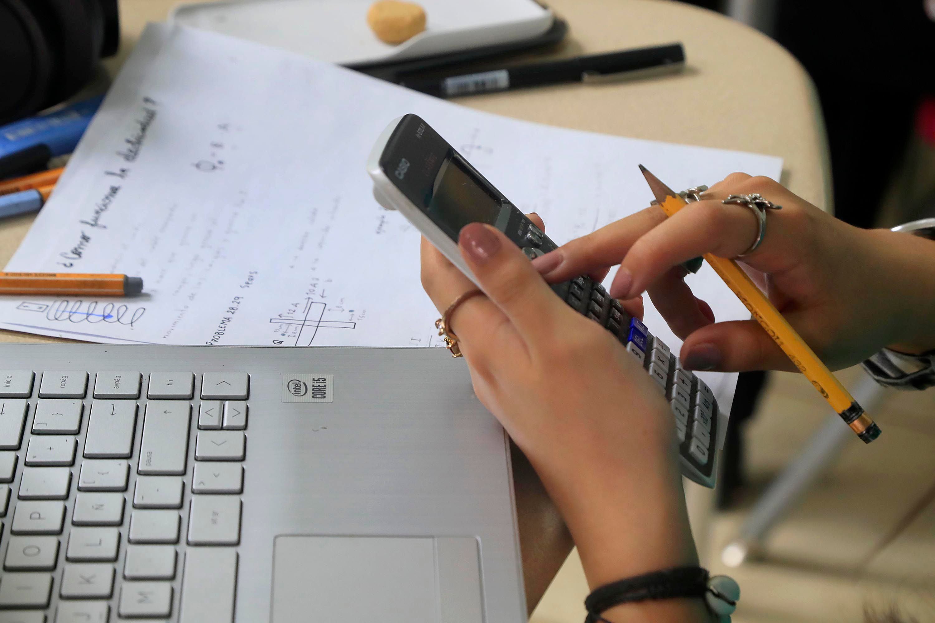 Una estudiante utiliza la calculadora para realizar ejercicios matemáticos frente a la computadora.