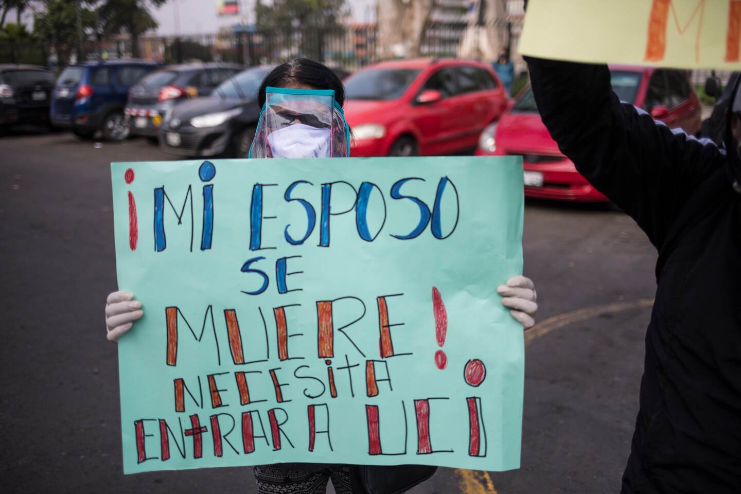 Daria Guerra wearing a face shield against the new coronavirus, holds a sign that reads in Spanish "My husband is dying. He needs to enter an intensive care unit," during a protest outside 2 de Mayo hospital in Lima, Peru, Thursday, May 14, 2020. (AP Photo/Rodrigo Abd)