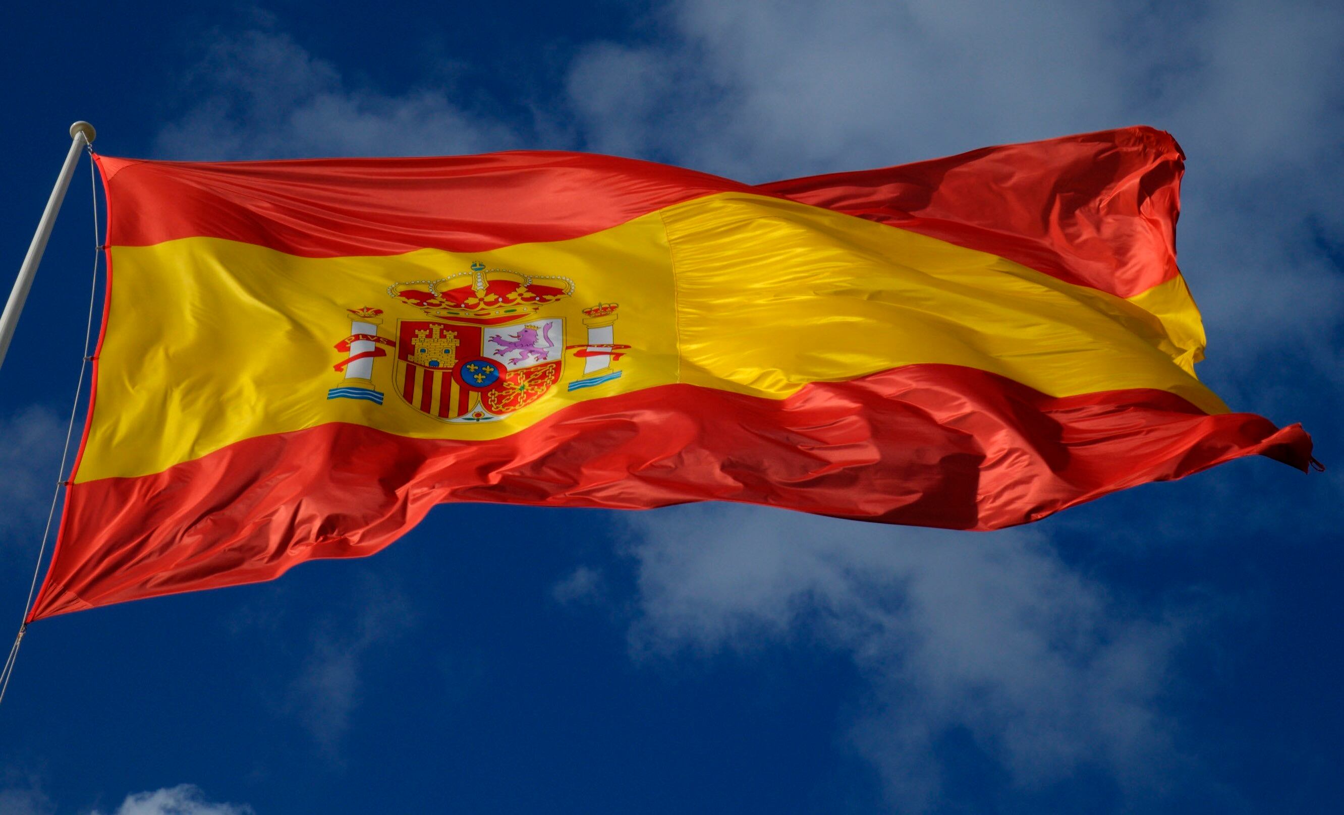 Una bandera de España ondea con un fondo azulado.