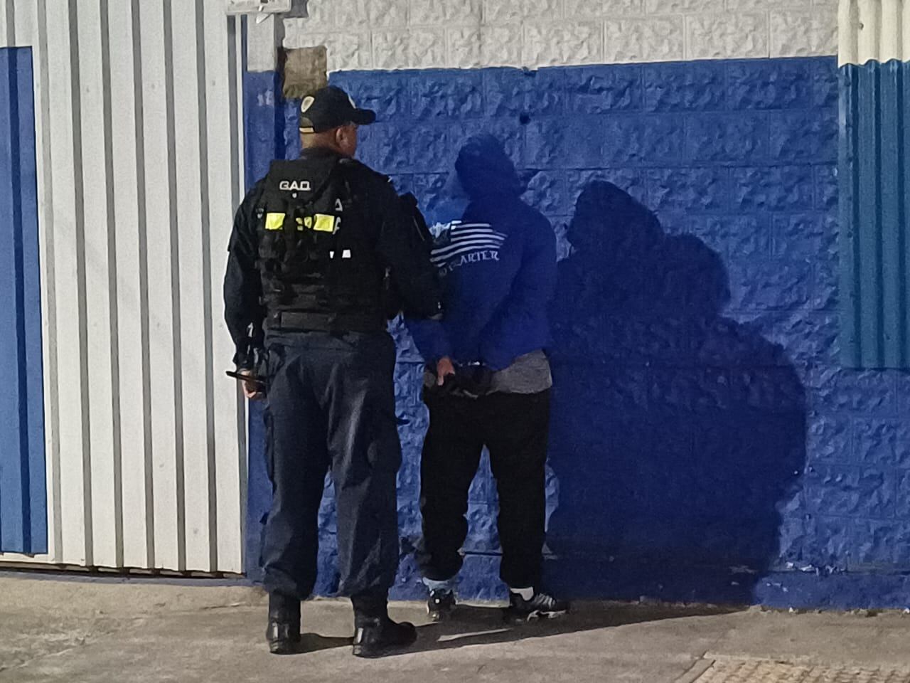 Un hombre, de espaldas, siendo capturado por un policía, también de espaldas.