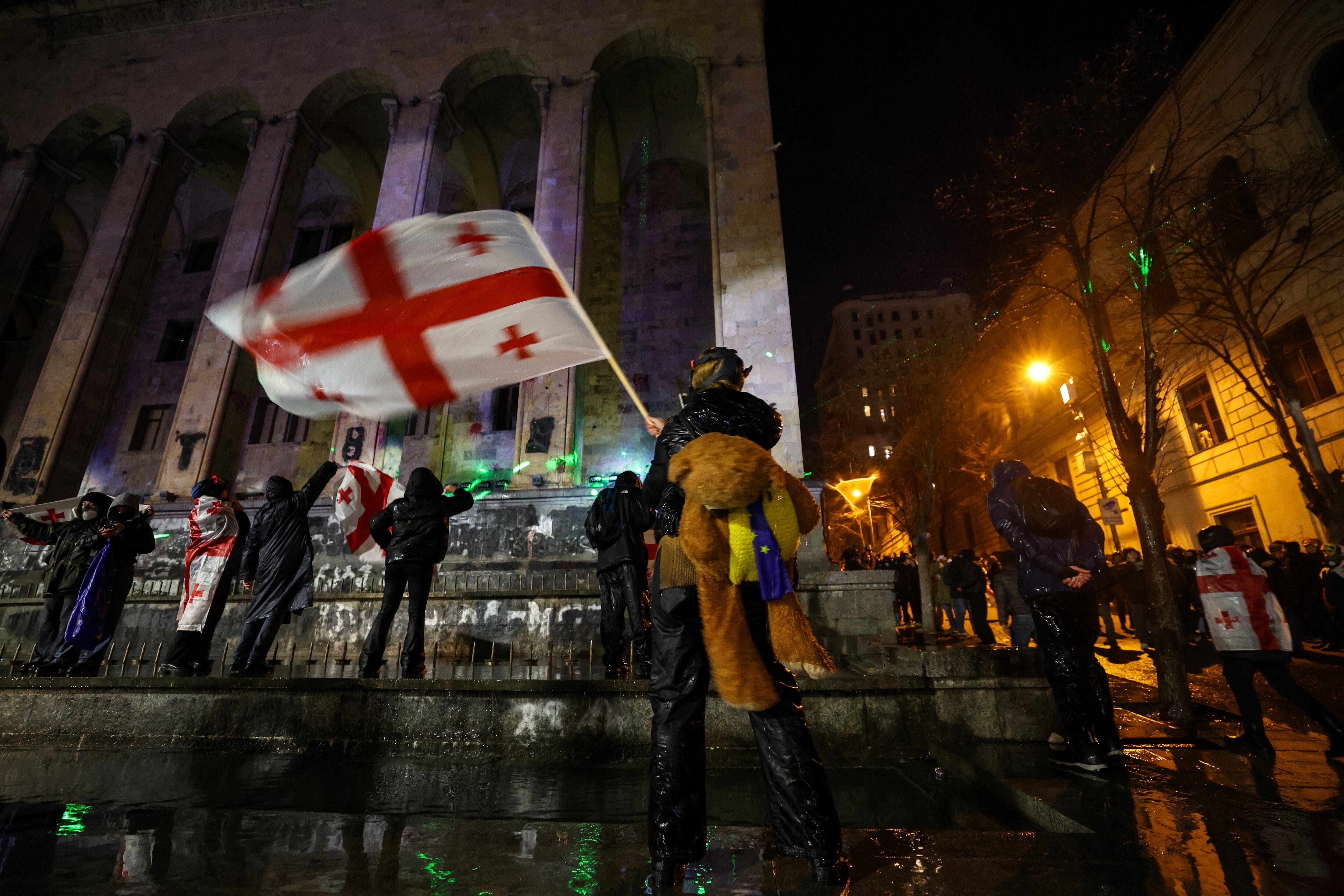 Personas protestando frente al Parlamento de Georgia en Tiflis, ondeando la bandera nacional y cargando símbolos proeuropeos, durante manifestaciones contra el gobierno prorruso.