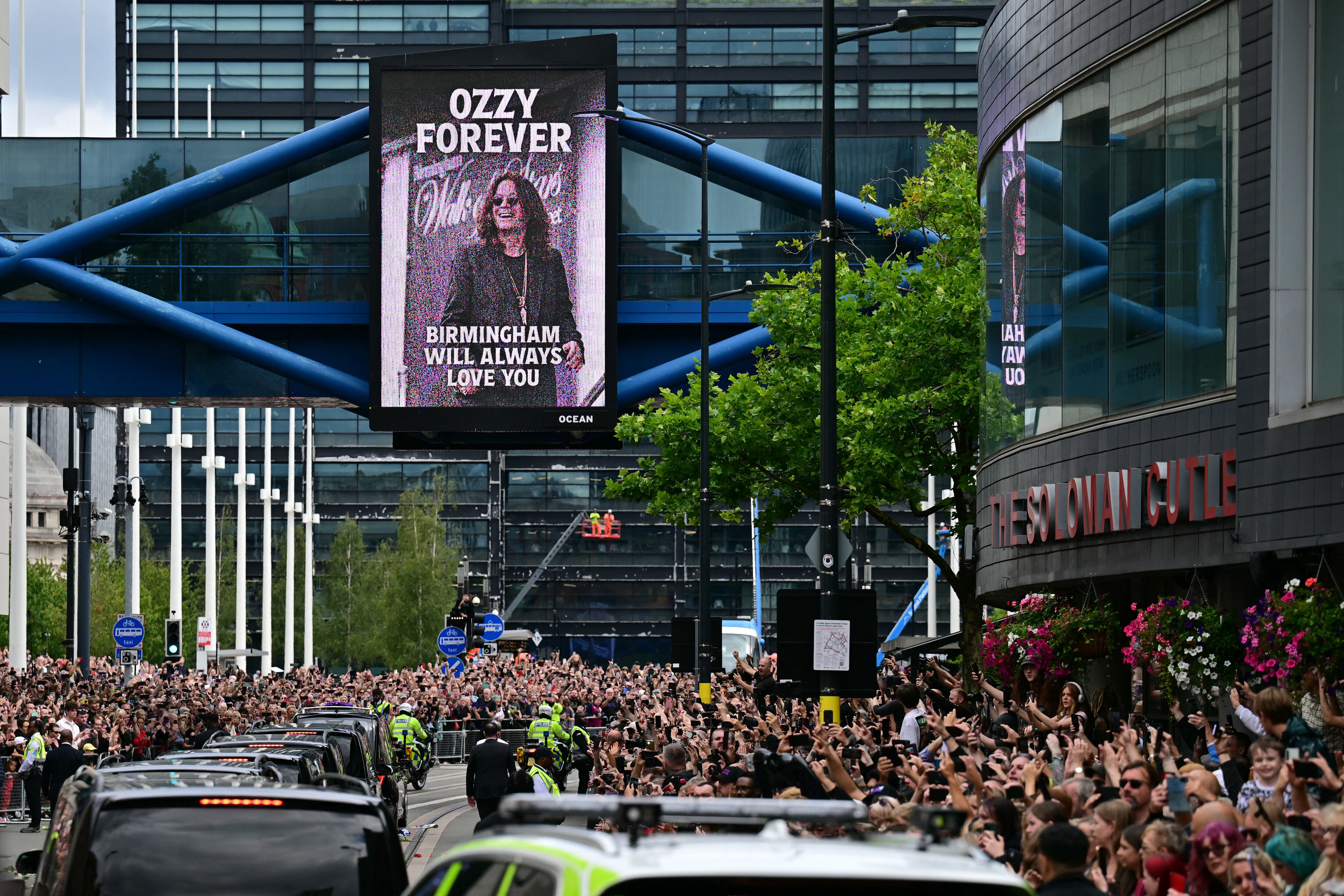 Mourners and music fans line the streets to pay their respects as the funeral cortege of Ozzy Osbourne, the late lead singer of Black Sabbath, makes its way through Birmingham, central England on July 30, 2025. Thousands are expected to line the streets in Ozzy Osbourne's UK hometown of Birmingham on Wednesday to honour the heavy metal hell-raiser Ozzy Osbourne as he is laid to rest. Osbourne, nicknamed the "Prince of Darkness" and who once bit a bat while on stage while performing with his Black Sabbath band, died on July 22 at the age of 76. (Photo by Ben STANSALL / AFP)