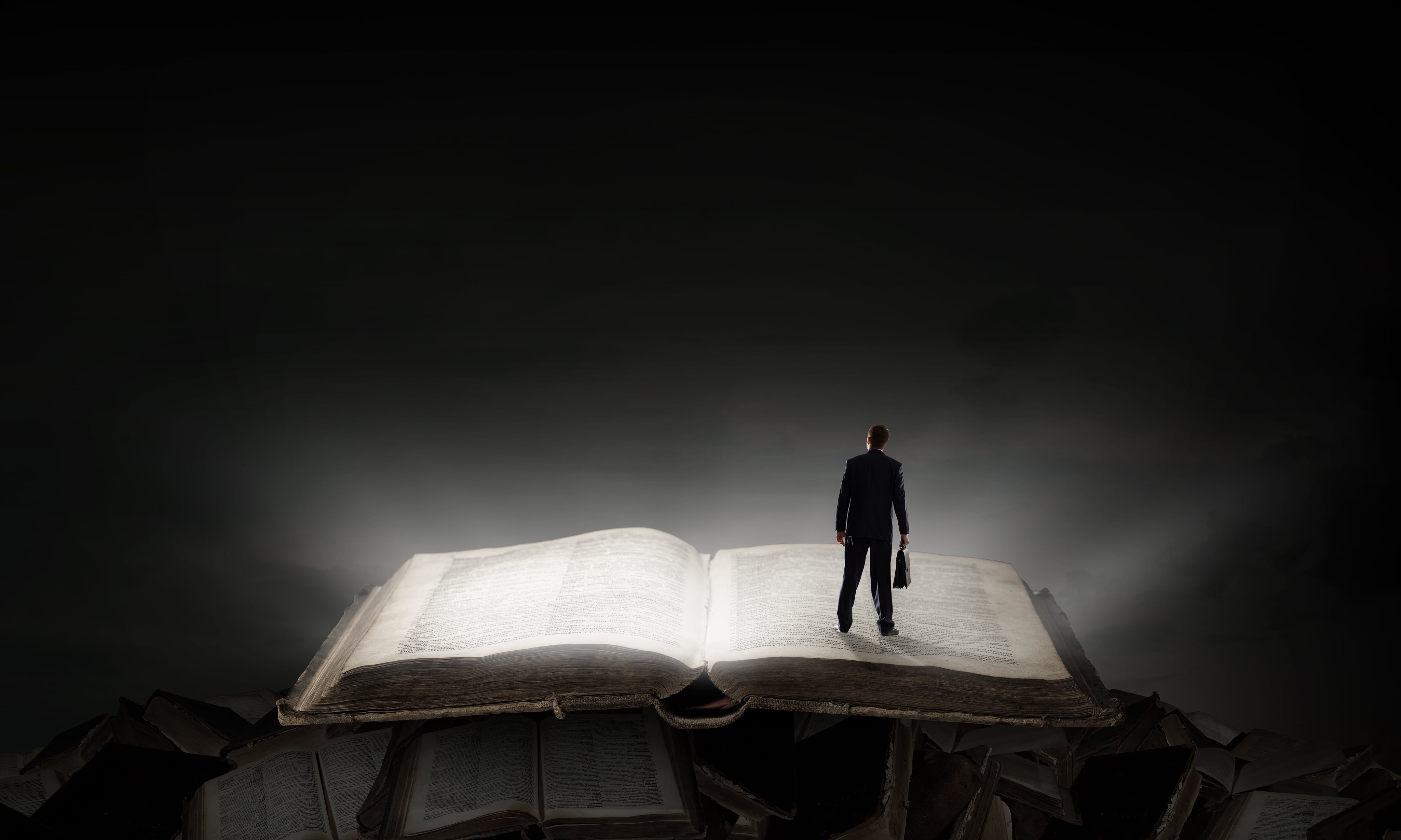 Hombre tamaño miniatura de pie sobre libro gigante, escena en penumbra