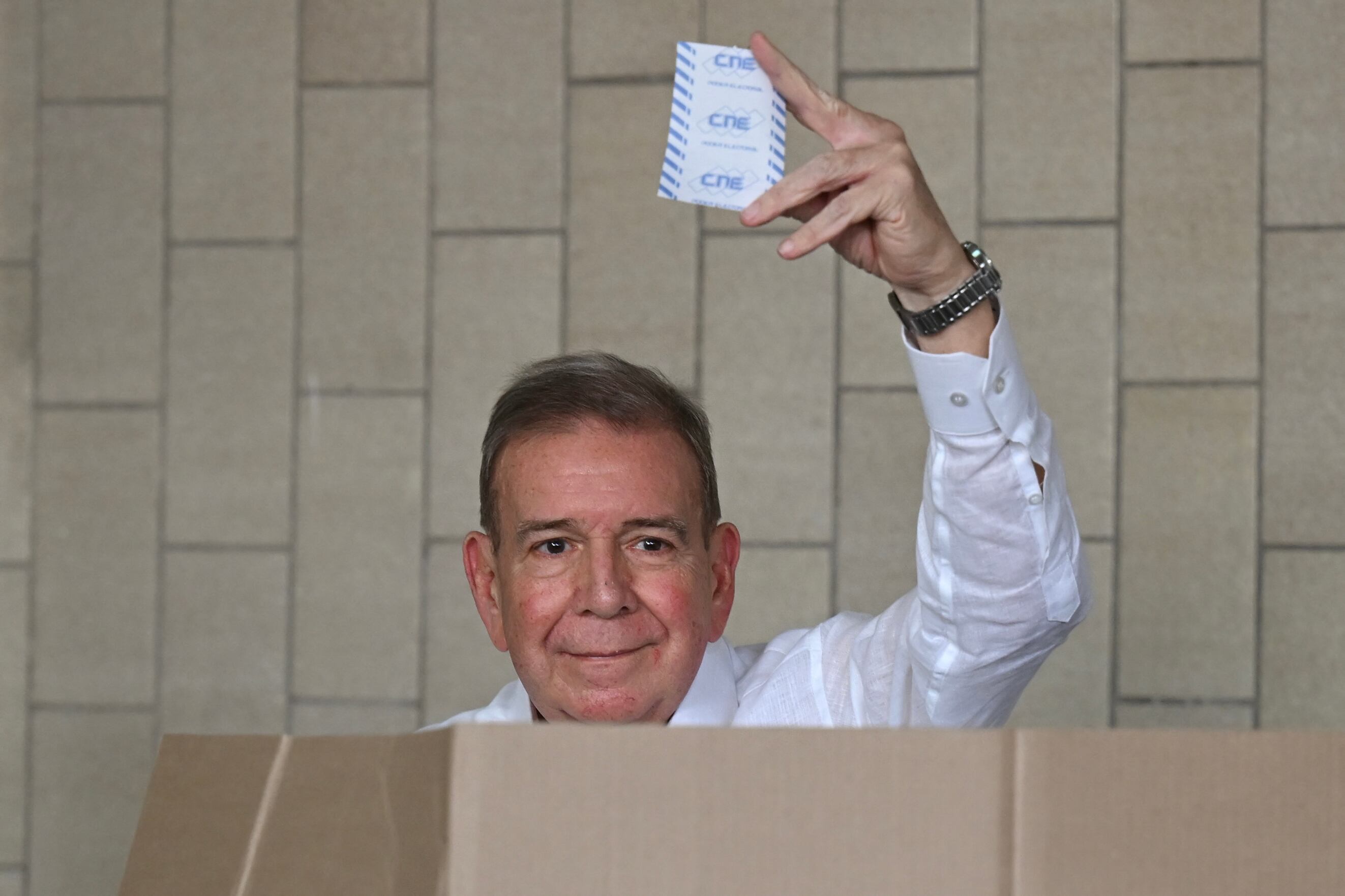 Edmundo González Urrutia sosteniendo su voto durante las elecciones presidenciales en Venezuela, sonriente y vestido de blanco.