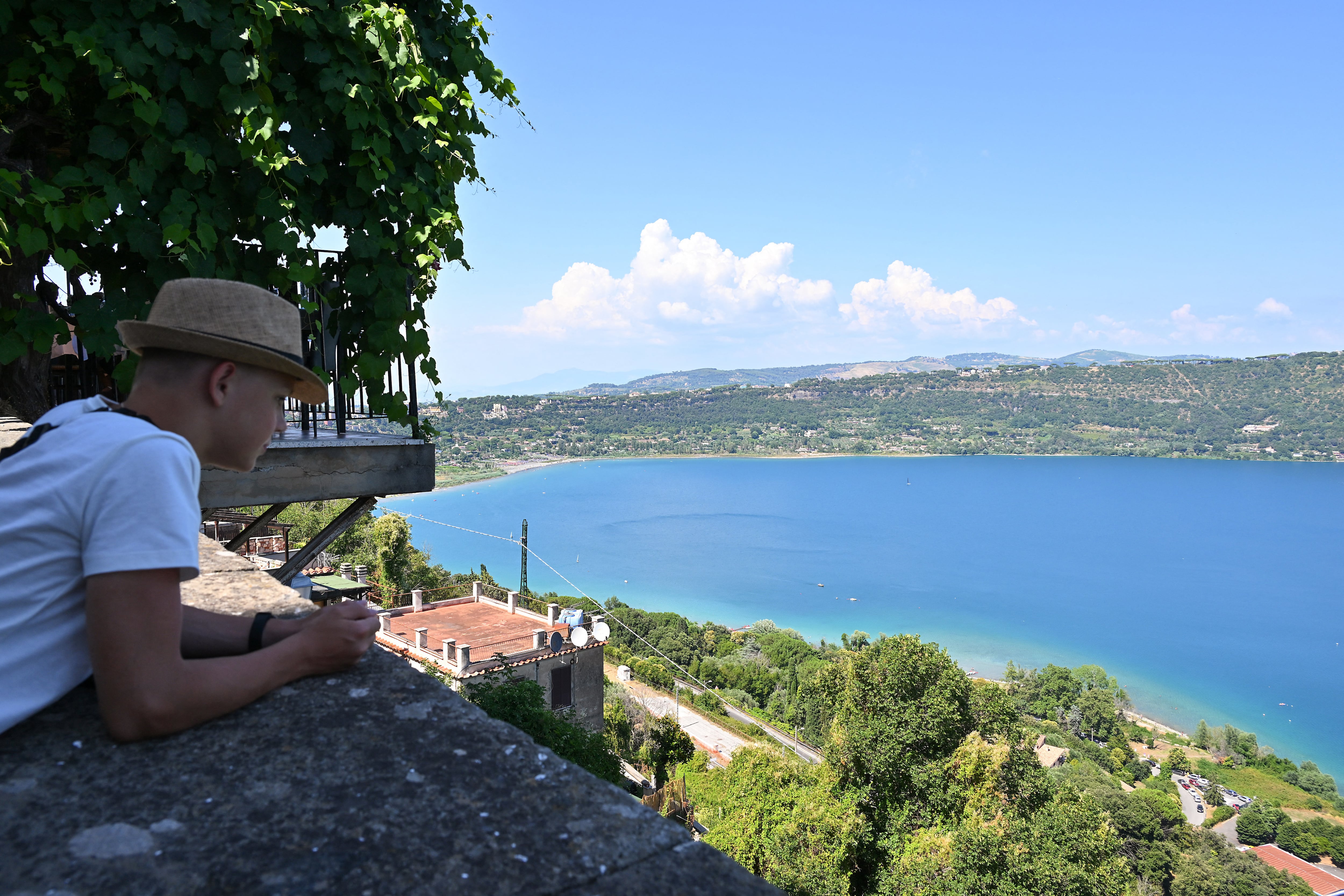 A man looks out at Albano lake in Castel Gandolfo, 40 km southeast of Rome, on July 6, 2025, ahead of the arrival of Pope Leone XIV for a two-week stay in the summer papal estate. The newly elected Pope Leo XIV, revives a long-standing papal tradition paused under Francis, as Castel Gandolfo prepares to welcome a pope for the first time in over a decade. (Photo by Andreas SOLARO / AFP)