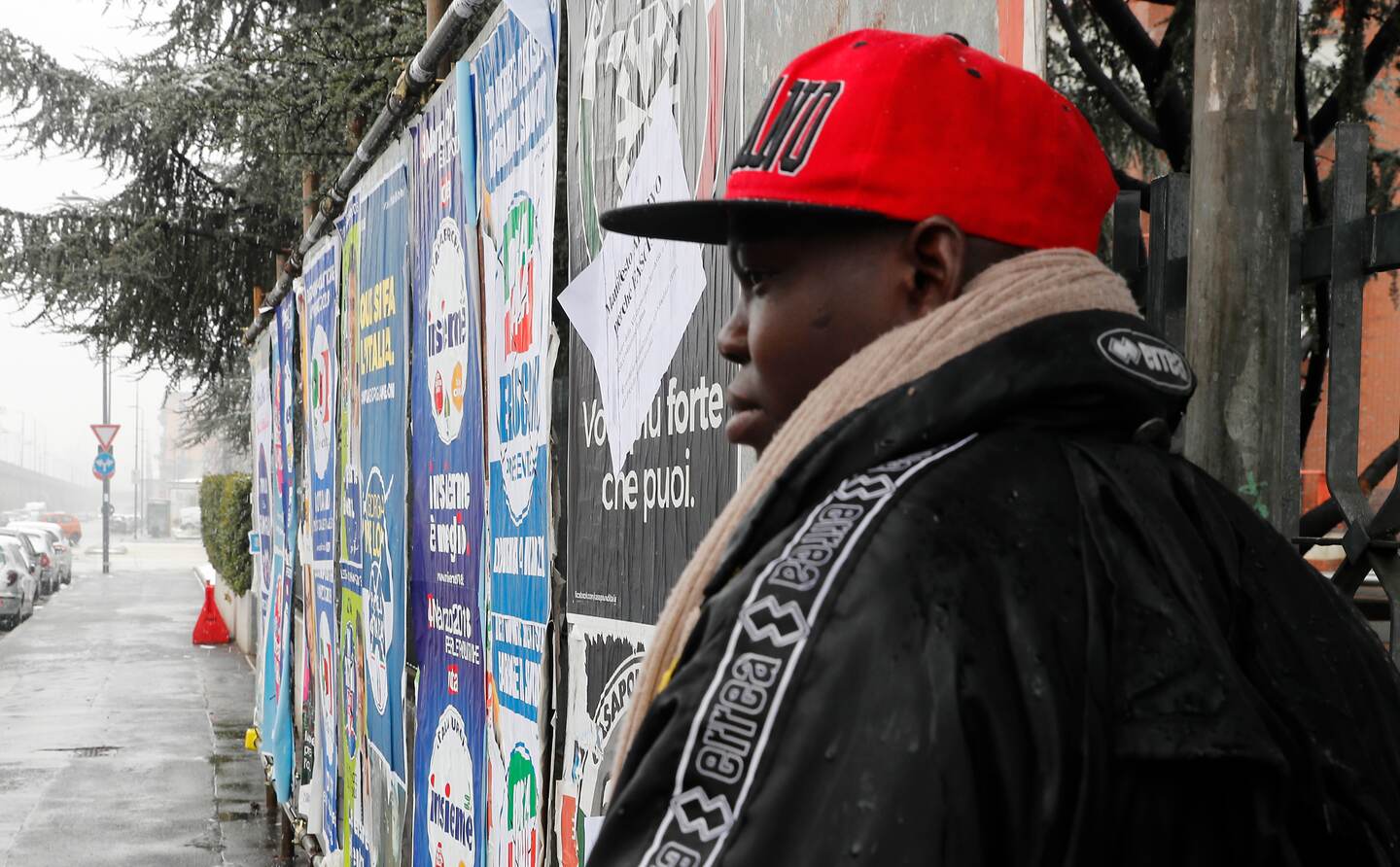 A man stands by electoral posters for Italy's general elections, in Milan, Italy, Saturday, March 3, 2018. An election in Italy on Sunday will determine the makeup of the nation's Parliament and its next government. (AP Photo/Antonio Calanni)