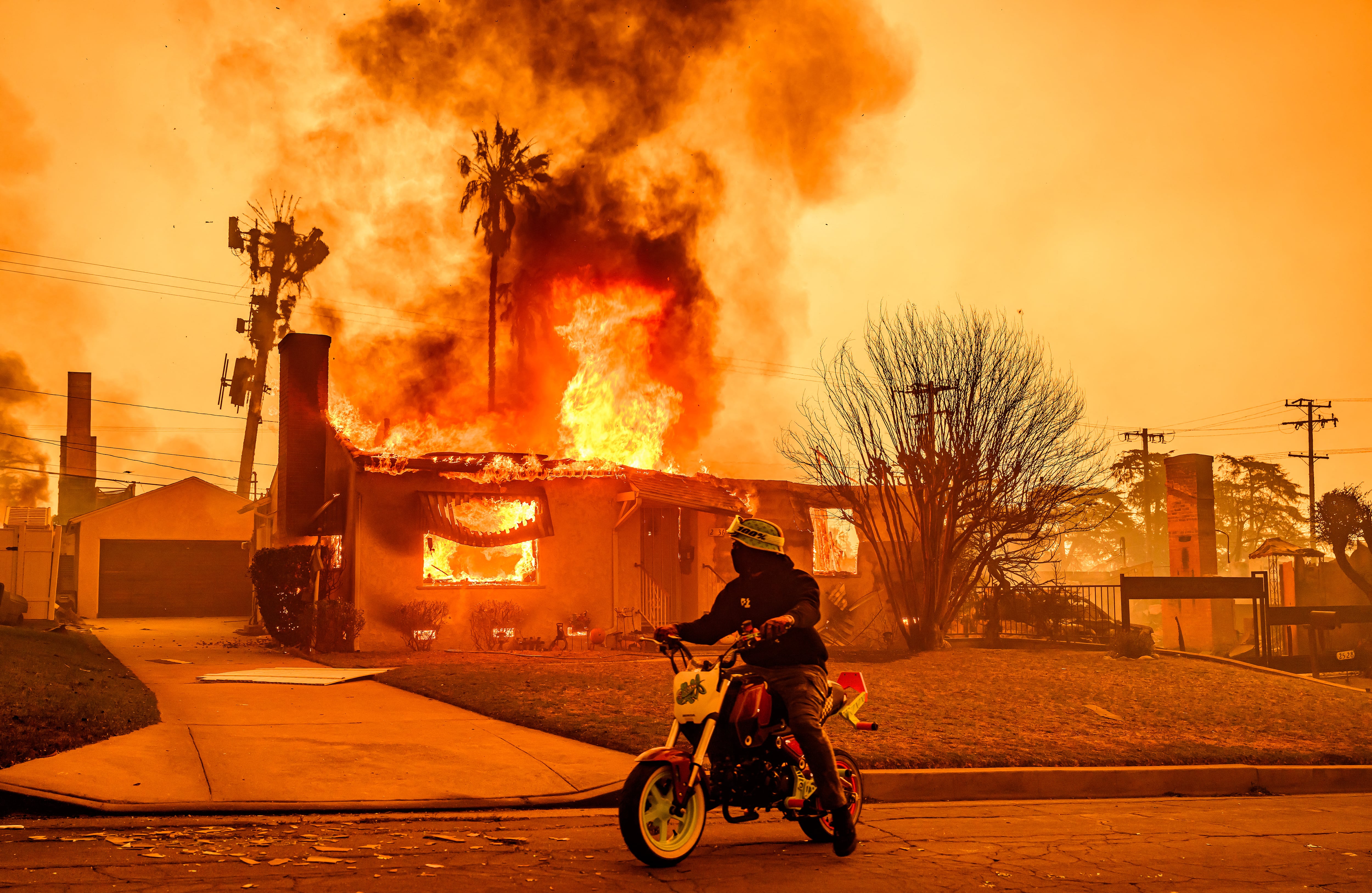 Un motociclista se detiene para mirar una casa en llamas durante el incendio de Eaton en el área de Altadena del condado de Los Ángeles, California