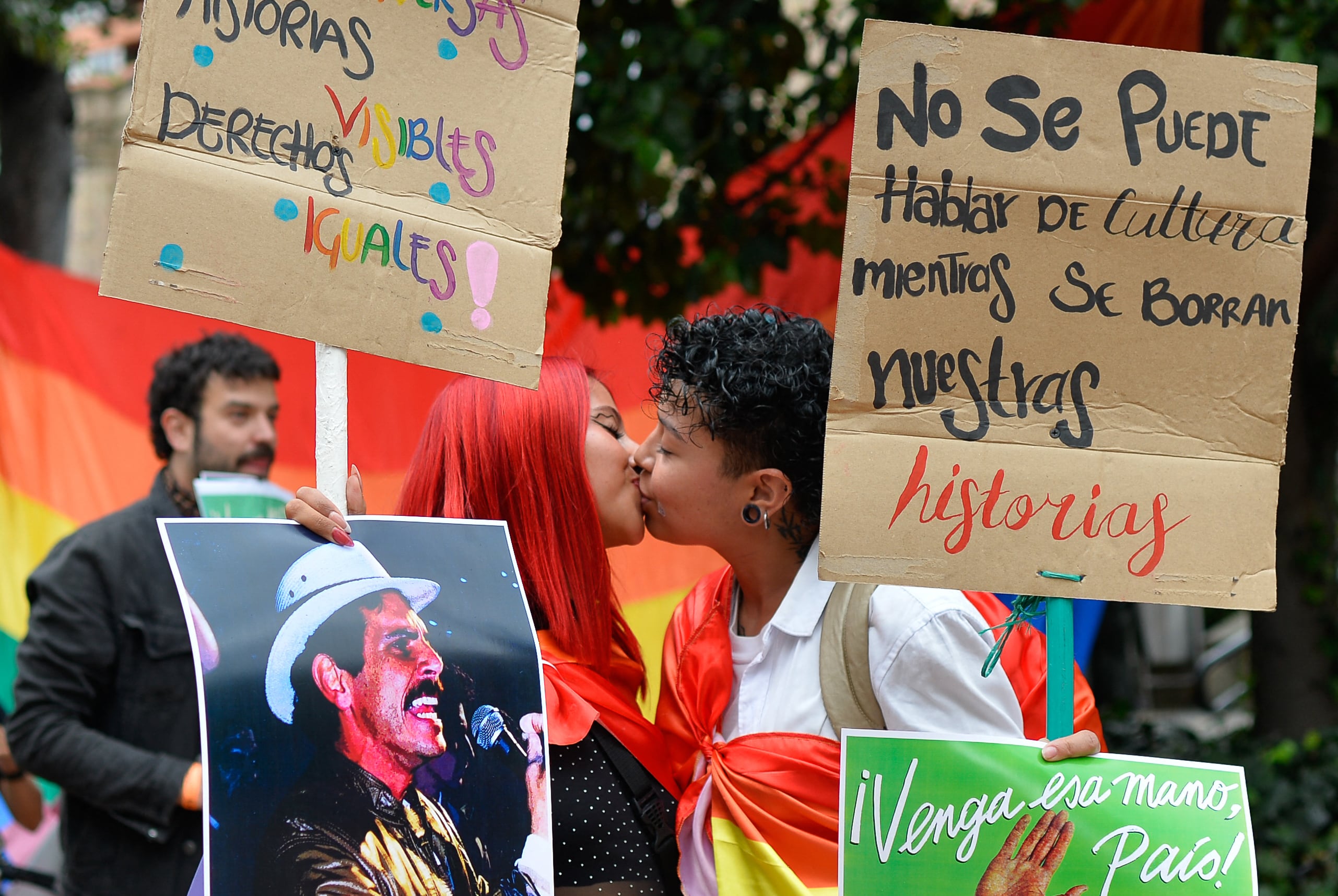 EDITORS NOTE: Graphic content / Demonstrators hold a picture of late leftist leader Carlos Pizarro, who was assassinated in 1990, as they kiss during a protest in front of National Museum against a government order to remove works alluding to LGBTQ rights and the country's peace process in Bogota on October 18, 2026. Colombia's new right-wing government has ordered one of the country's top museums to remove dozens of works alluding to LGBTQ rights and the country's peace process, sparking condemnation from visitors. (Photo by Sebastian BARROS / AFP)