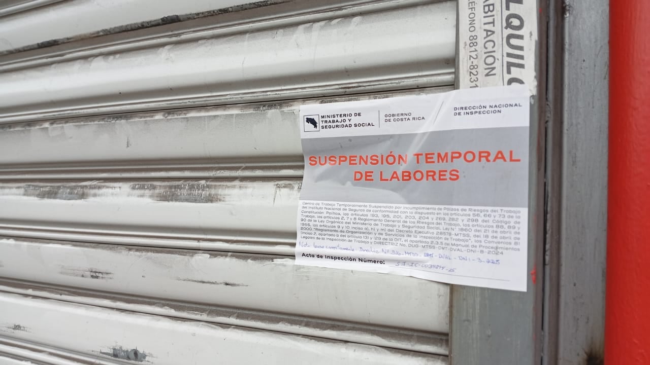 Un portón cerrado, lleva pegado un rótulo que dice "Suspensión temporal de labores".