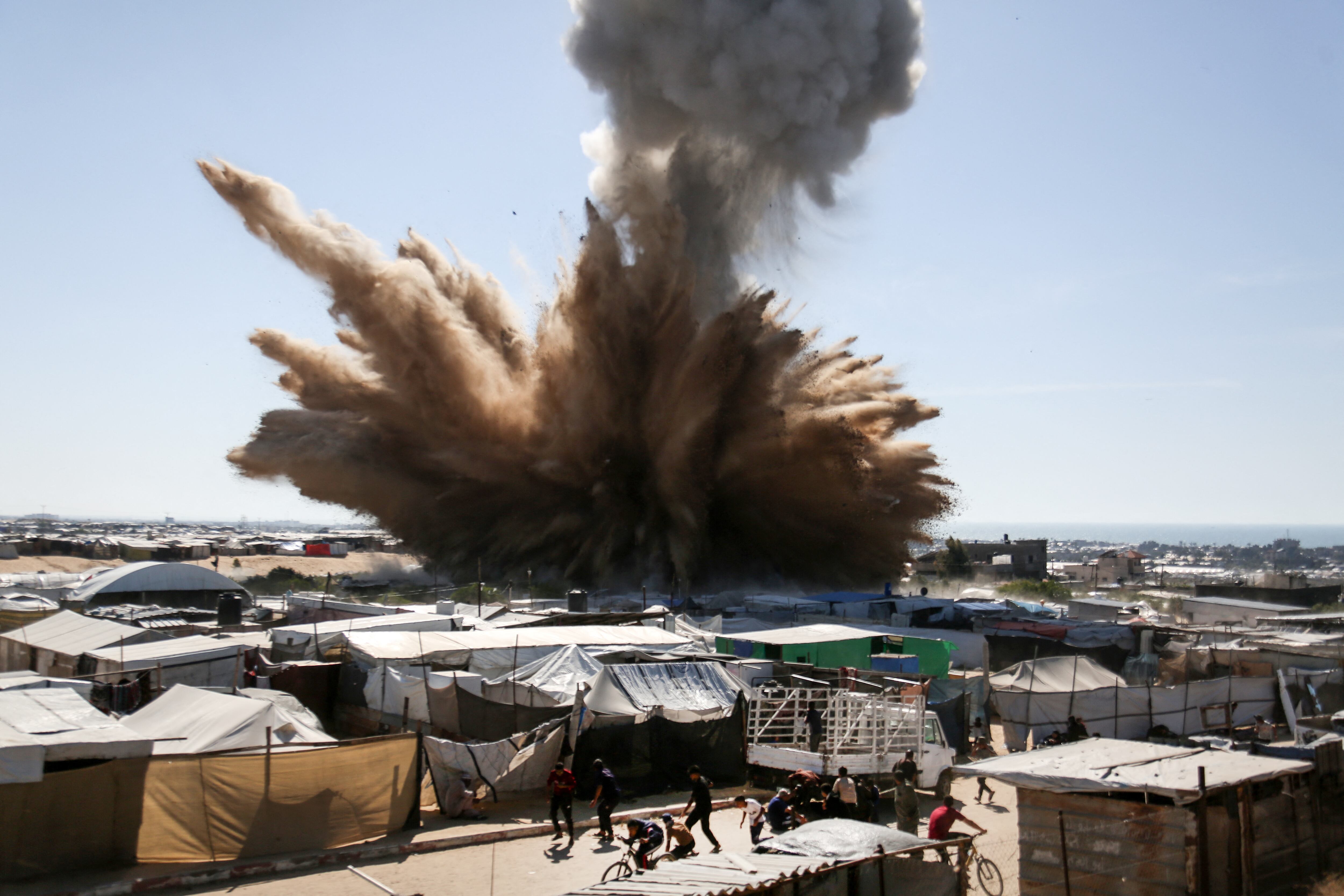 People run for cover as a plume of smoke rises above tents at a camp for displaced Palestinians in northern Khan Yunis in the southern Gaza Strip, during an Israeli strike on April 19, 2025. (Photo by AFP)