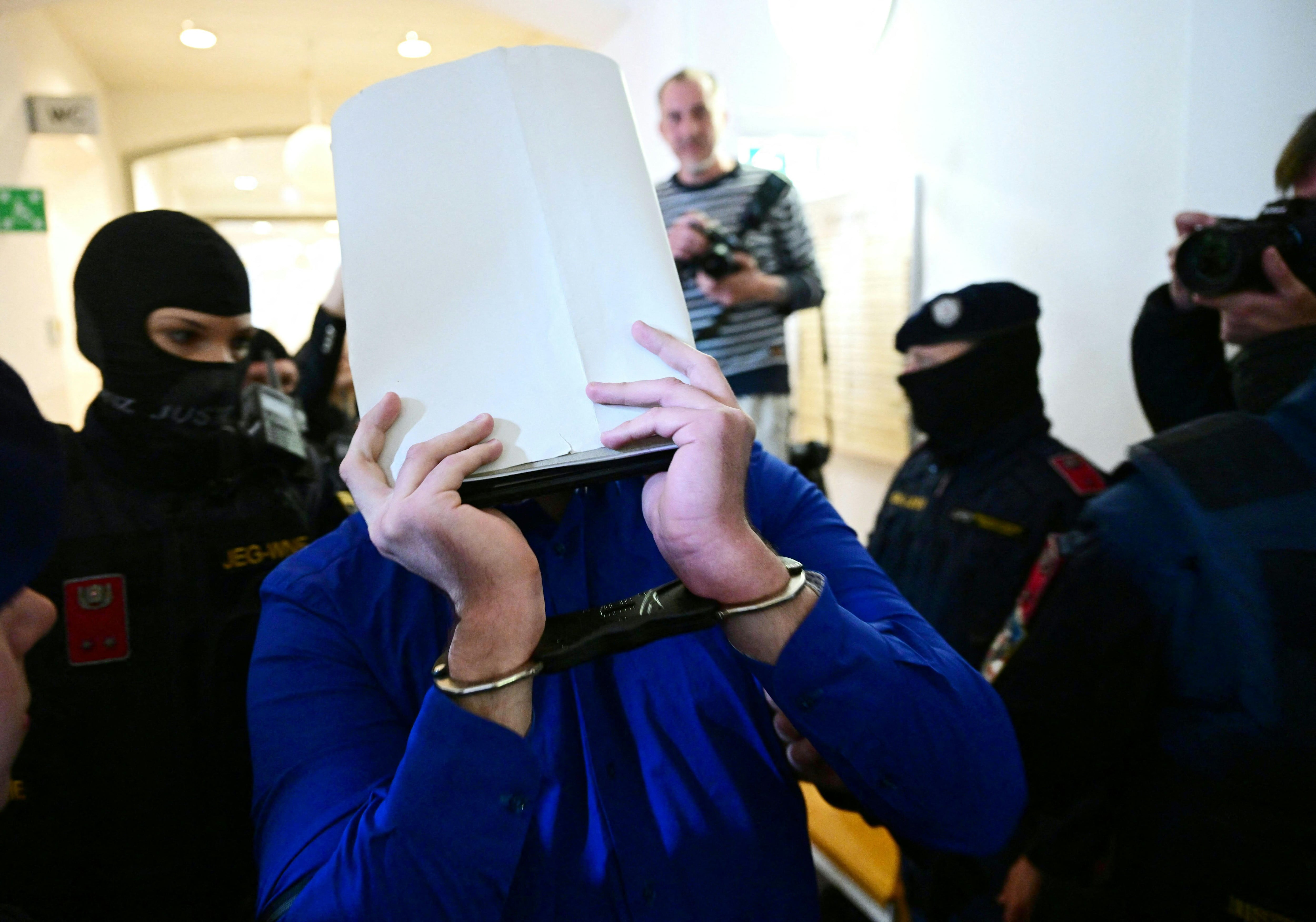 Un acusado esposado es escoltado a la sala del tribunal por agentes judiciales al comenzar el juicio en un juzgado de Wiener Neustadt, Austria, el 28 de abril de 2026, por un complot para atacar un concierto de Taylor Swift en Viena.