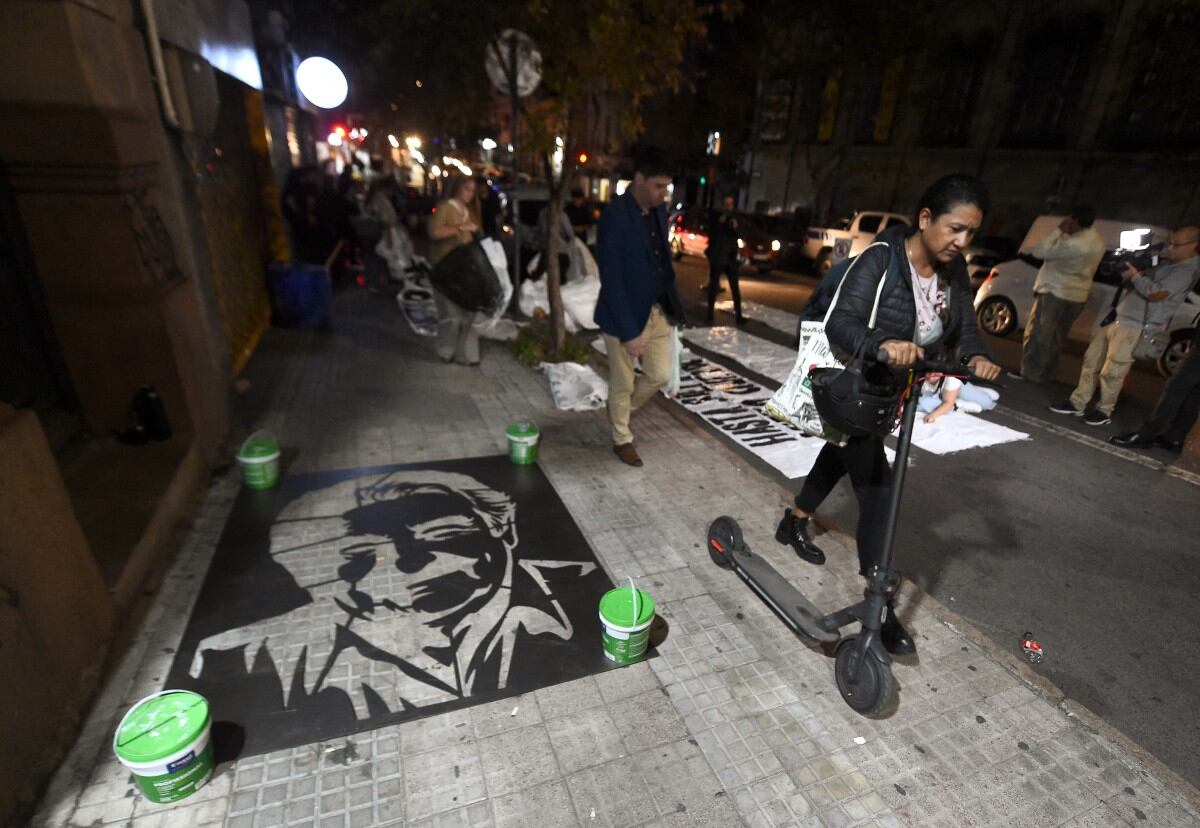 People walk past as people prepare to paint the image of late Uruguay's President Jose Mujica in the floor in Montevideo on May 13, 2025. Uruguay's former president (2010-2015) Jose Mujica, a former guerrilla fighter and icon of the left in Latin America, died at the age of 89 on May 13, 2025, the government announced. The farmer dubbed the "world's poorest president" during his presidency for his modest lifestyle had been diagnosed with cancer of the esophagus in May 2024. (Photo by DANTE FERNANDEZ / AFP)