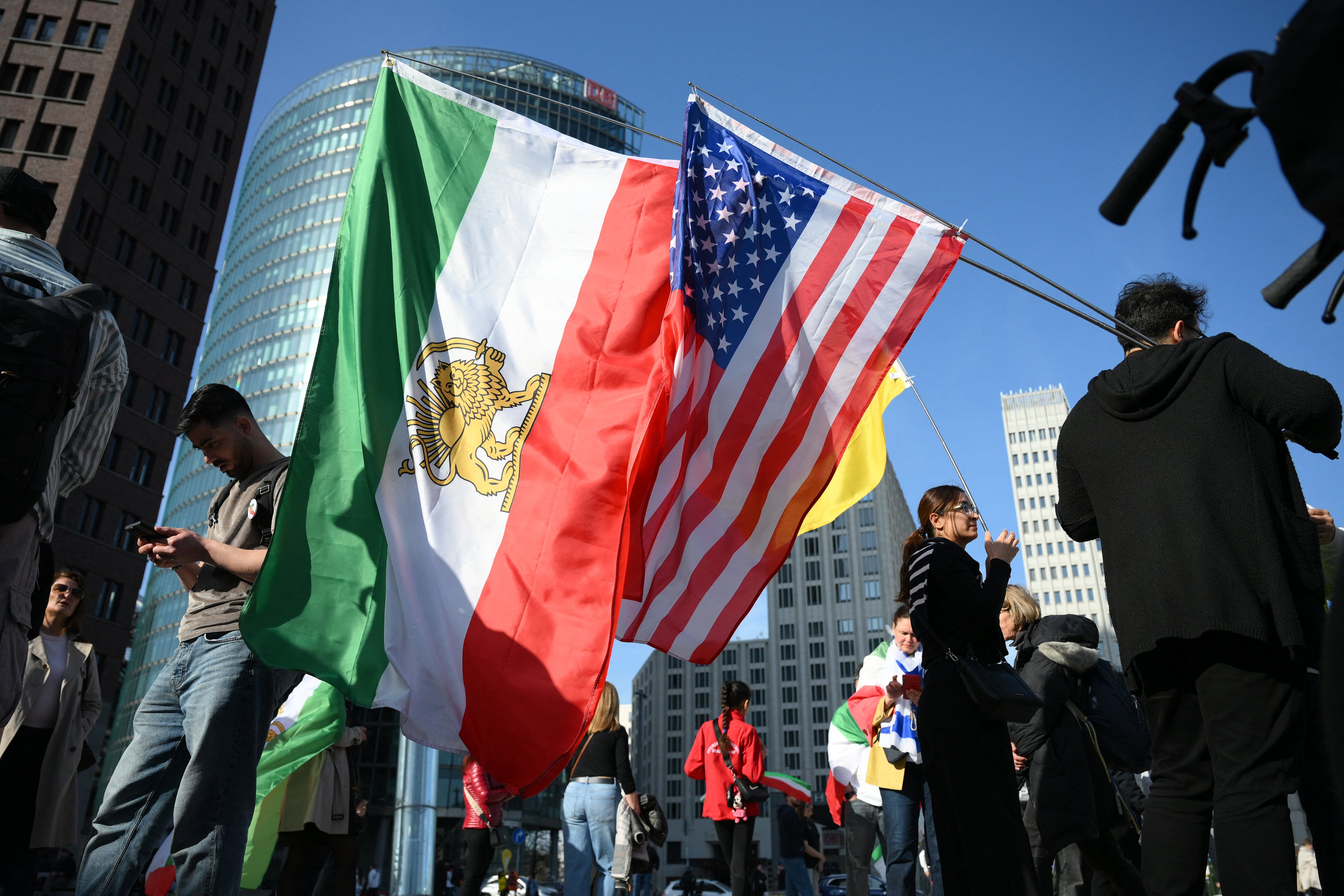 La gente protesta mientras se ven banderas iraníes pre-revolucionarias con el león y el sol junto a banderas estadounidenses durante una manifestación por la «Libertad para Irán» en la plaza Potsdamer Platz de Berlín, Alemania, el 28 de febrero de 2026. Estados Unidos e Israel lanzaron ataques contra Irán el 28 de febrero, lo que desató el temor a una guerra regional con explosiones en todo Oriente Medio, ya que la República Islámica respondió con una lluvia de misiles.