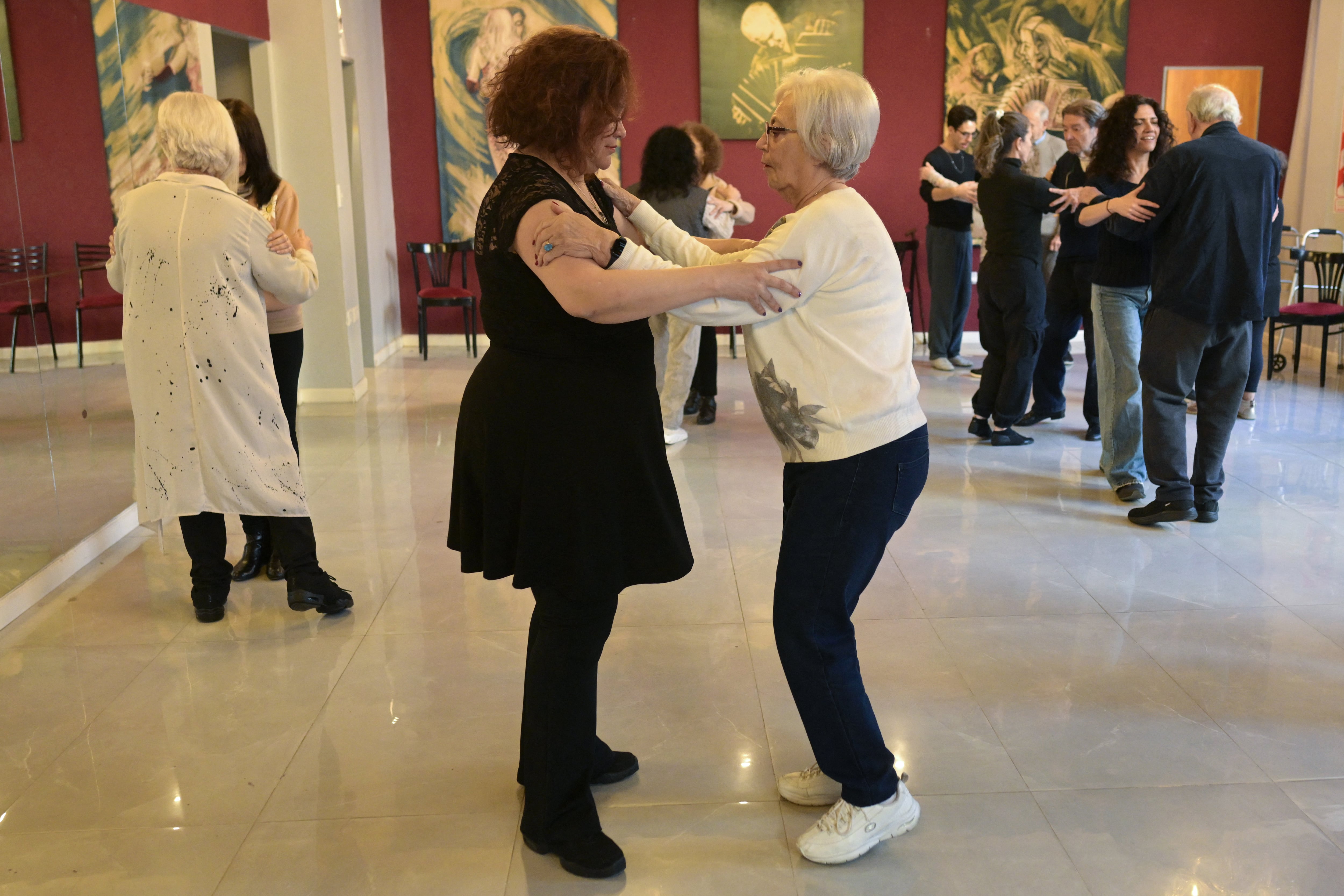 Una mujer adulta mayor que padece la enfermedad de Parkinson baila con la profesora de tango Verónica Alegre durante una sesión de terapia con tango en Buenos Aires, el 26 de agosto de 2025. Unos 200 pacientes han participado en los talleres semestrales de tango organizados desde hace 15 años por el hospital público Ramos Mejía de Buenos Aires, cuyo objetivo es estudiar su impacto en la progresión de esta enfermedad neurodegenerativa incurable y brindar herramientas de rehabilitación, informaron a la AFP los neurólogos a cargo. (Foto: Juan Mabromata / AFP)