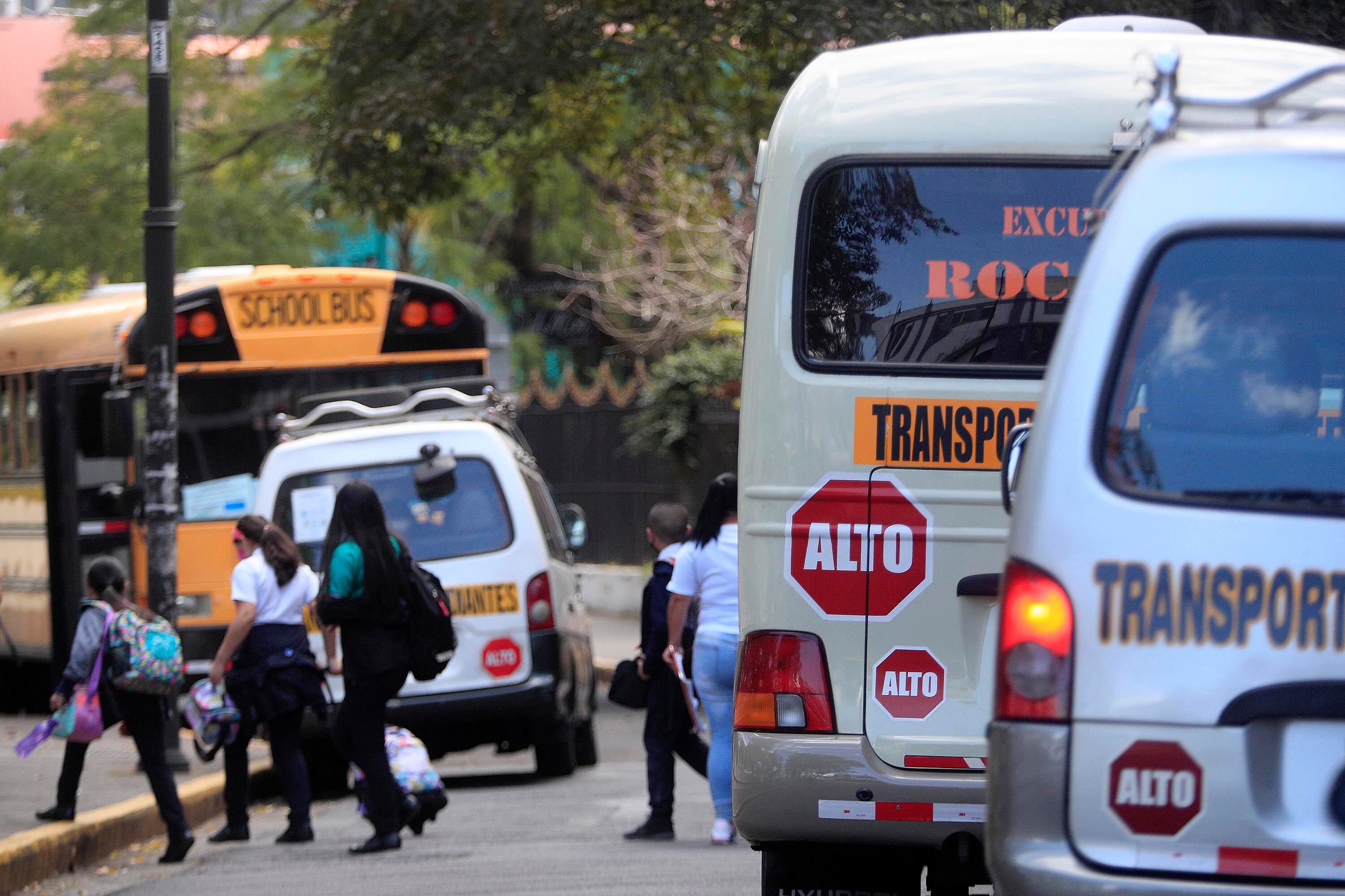 Microbuses y buses de transporte de estudiantes en Costa Rica, estacionados junto a escolares caminando.