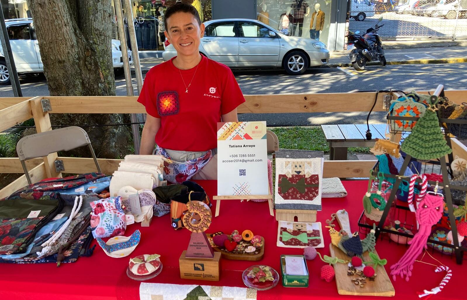 Una mujer de pie con productos sostenibles como bolsos, canguros y artículos de crochet diseñados para fomentar la sostenibilidad.