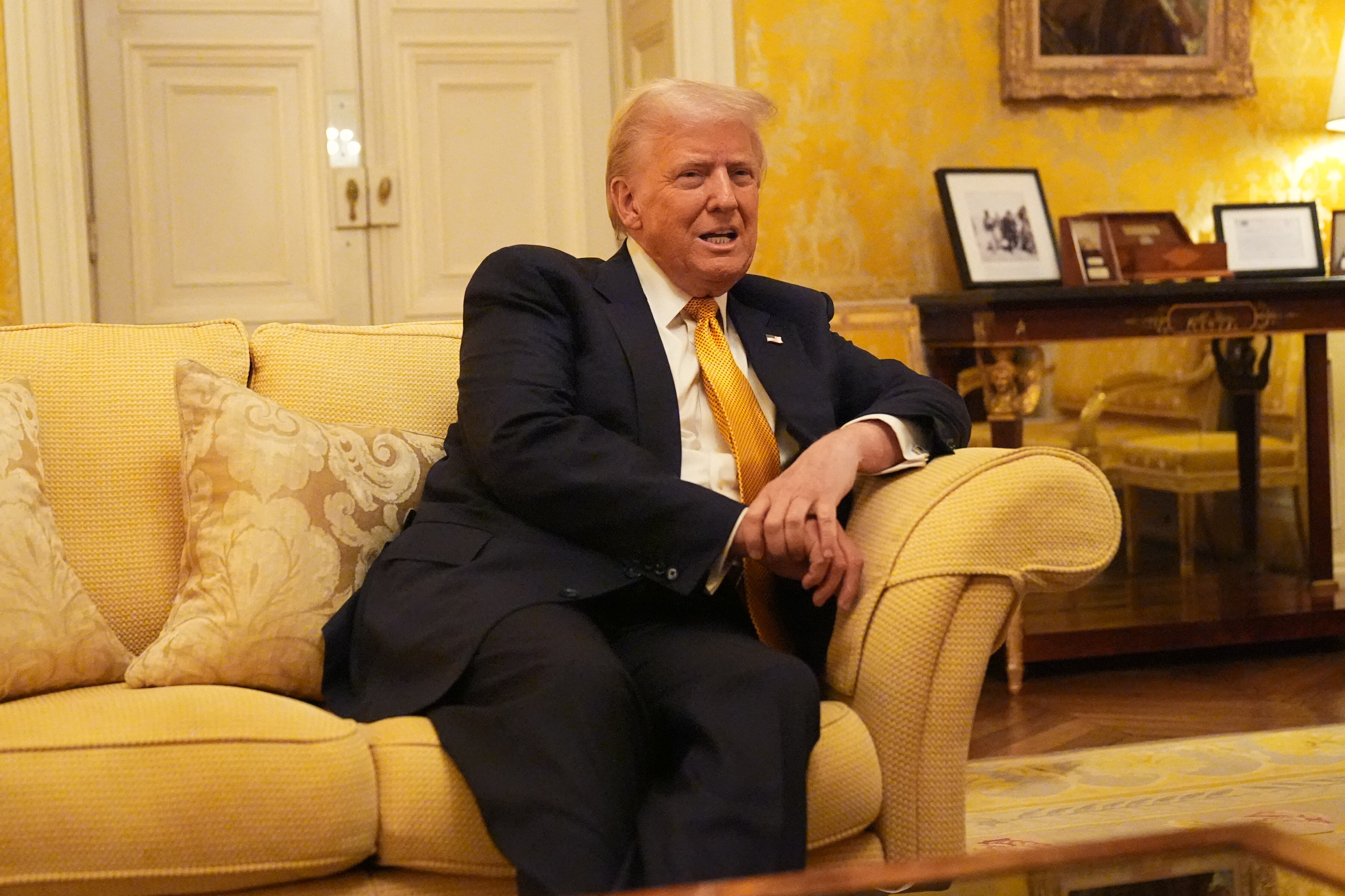 El expresidente Donald Trump aparece relajado y sonriente, sentado en un sofá decorativo en un entorno diplomático. La imagen captura un momento clave de una reunión formal en el ámbito político.