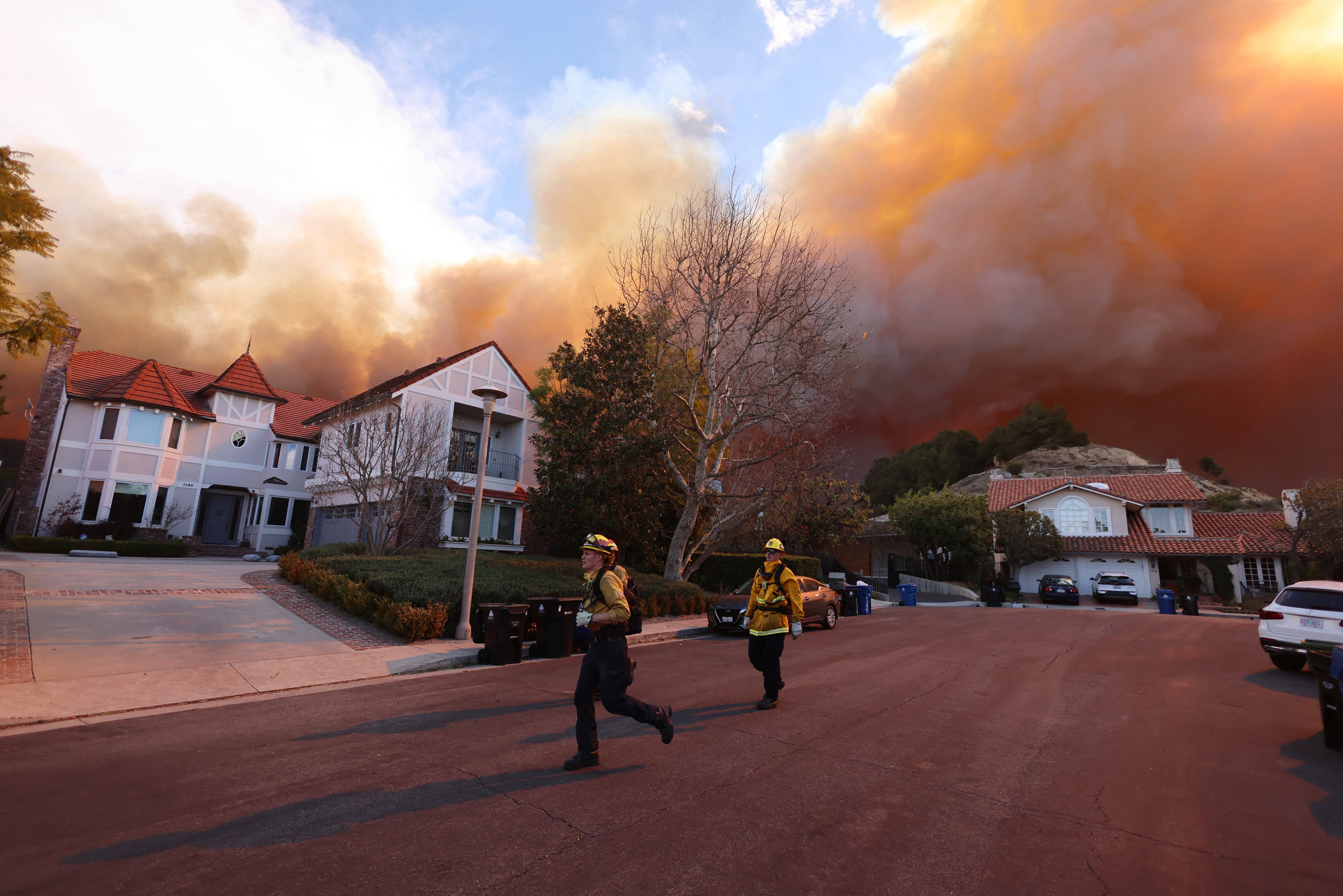Los bomberos corren mientras arde un incendio forestal en Pacific Palisades, California.