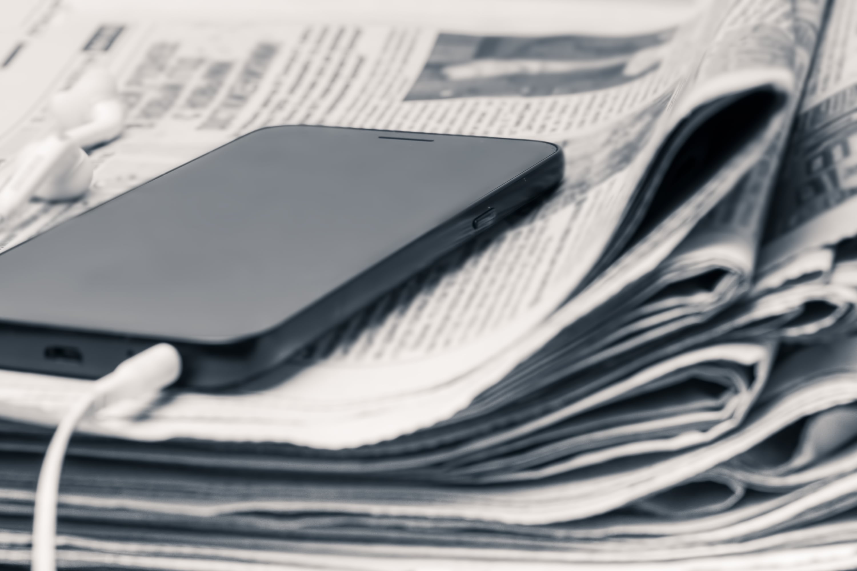 Prensa escrita, periódicos, y transición al periodismo digital, celular cargándose. Teléfono celular sobre periódicos doblados
