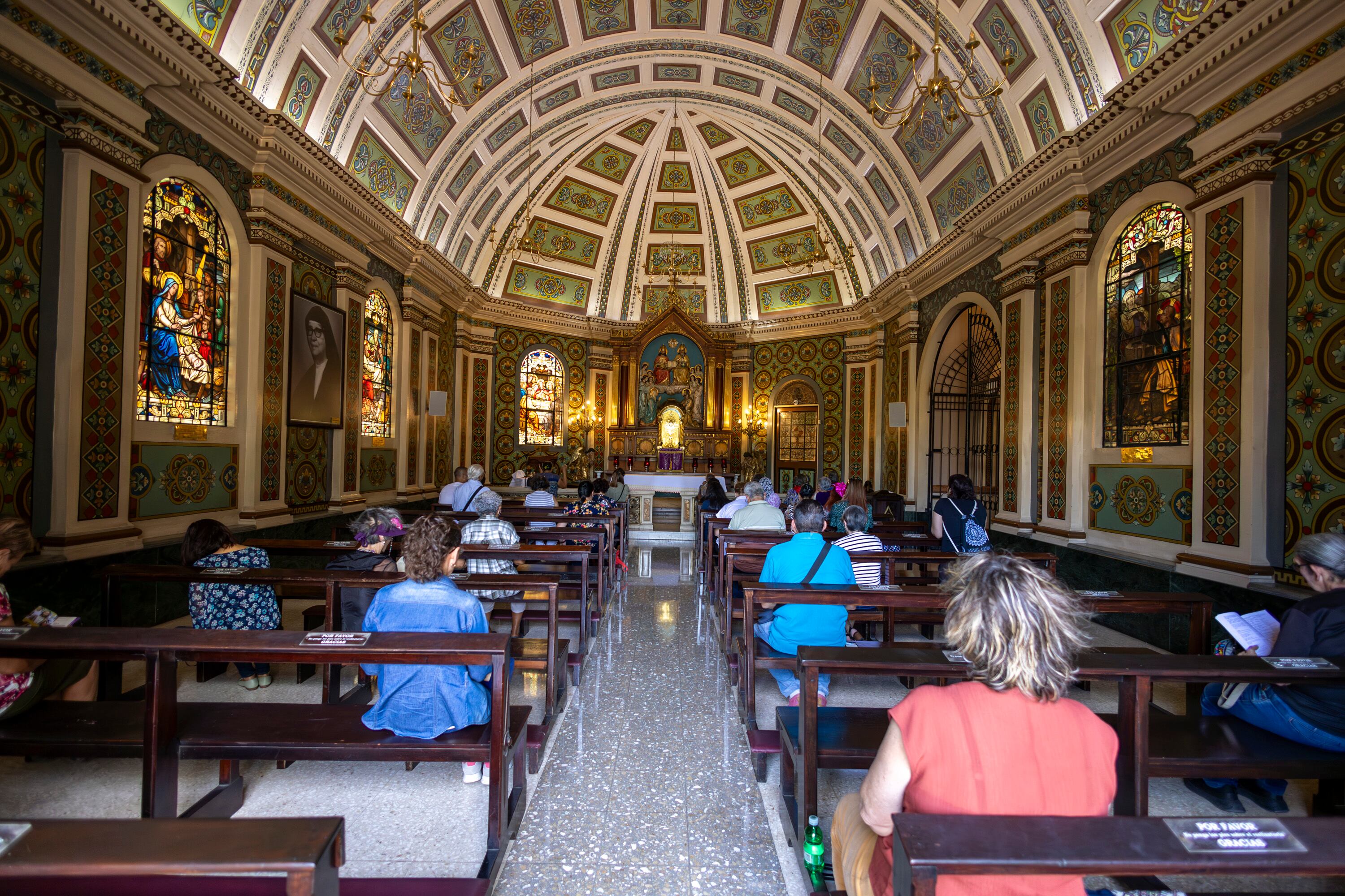 Imagen del interior de la catedral metropolitana visto desde atrás: con personas de espaldas, sentadas en las bancas. Al fondo, iluminado, el altar.