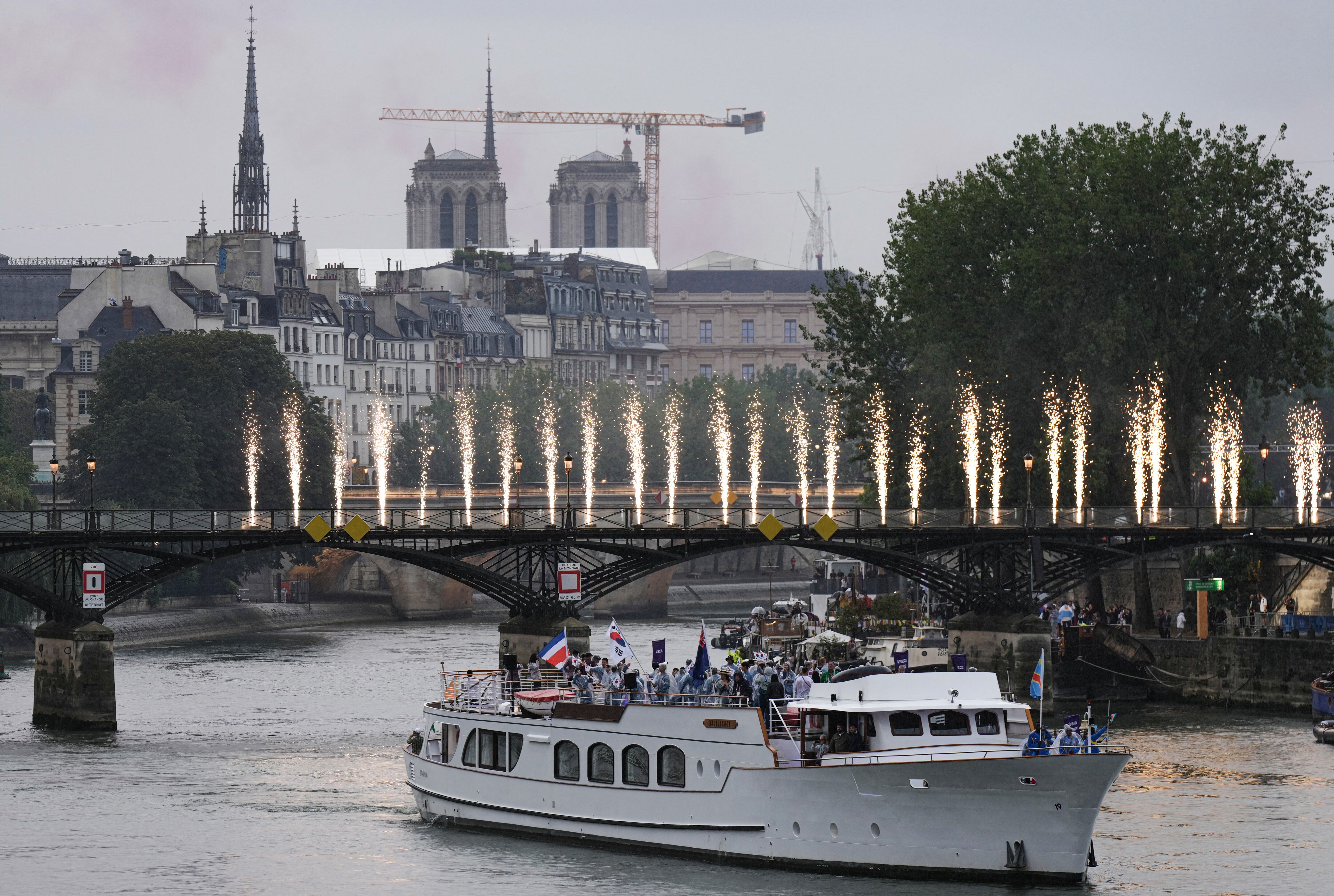 Atletas de las delegaciones de la República Democrática del Congo (de derecha a izquierda), Islas Cook, Corea del Sur y Costa Rica navegan en un bote por el río Sena, pasando por el puente peatonal Pont des Arts iluminado con fuegos artificiales, durante la ceremonia de apertura de los Juegos Olímpicos de París 2024 en París, el 26 de julio de 2024.