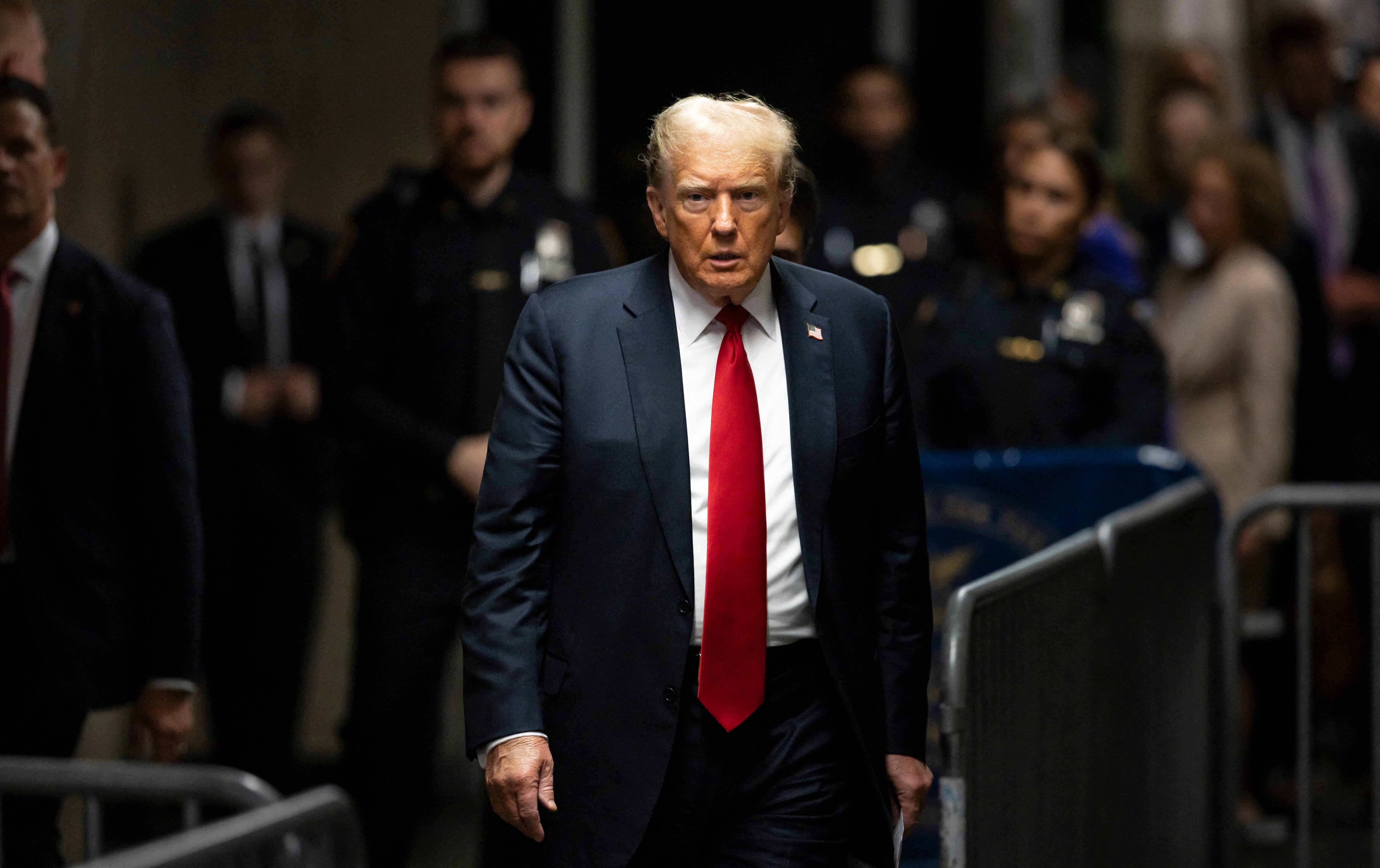 Donald Trump caminando escoltado en un lugar público, vestido con traje oscuro y corbata roja, en una fotografía de archivo tomada durante uno de sus procesos legales en 2023.