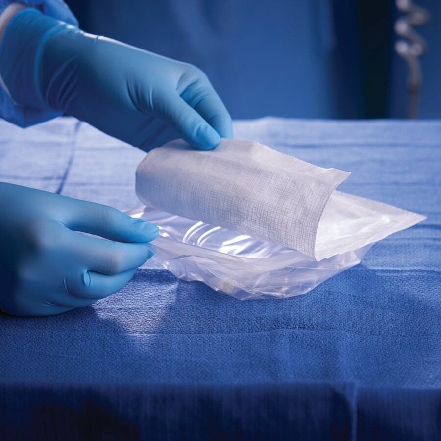 Manos con guantes azules manipulan un empaque estéril sobre una mesa quirúrgica, como parte del proceso de producción de DuPont en Heredia para la industria de dispositivos médicos.