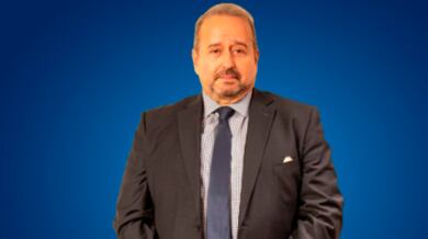 Retrato de hombre mayor, con barba, con traje entero oscuro. Fondo azul.