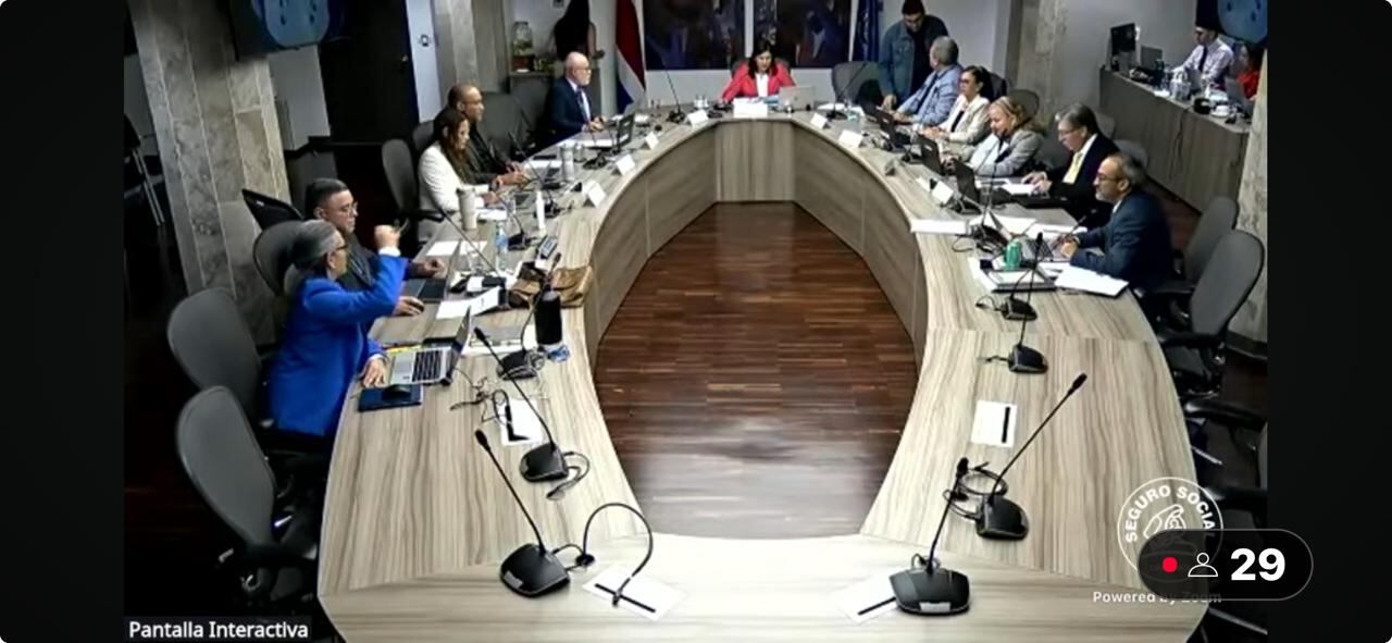 Salón con mesa oval y personas sentadas alrededor.