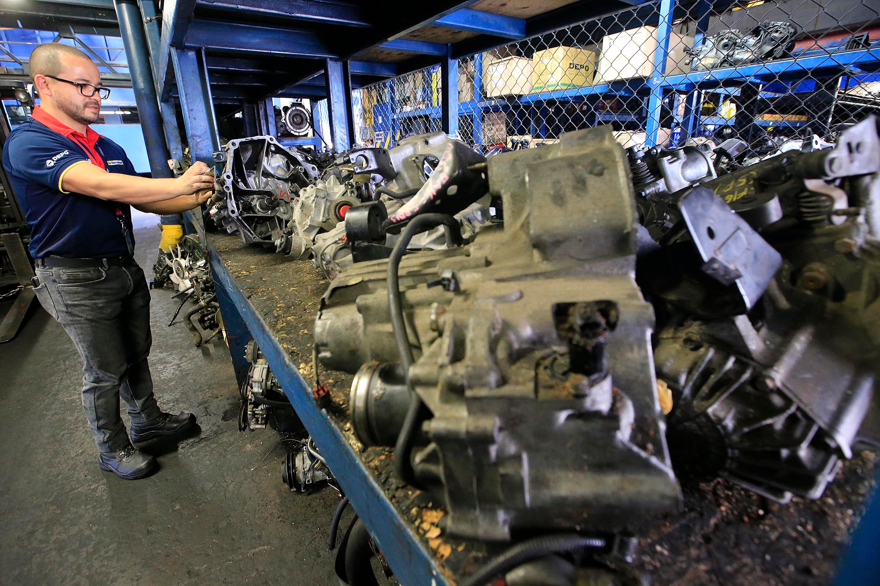 Hombre revisando repuestos automotrices en un taller de distribución en Costa Rica, con piezas de motores y transmisiones en exhibición.