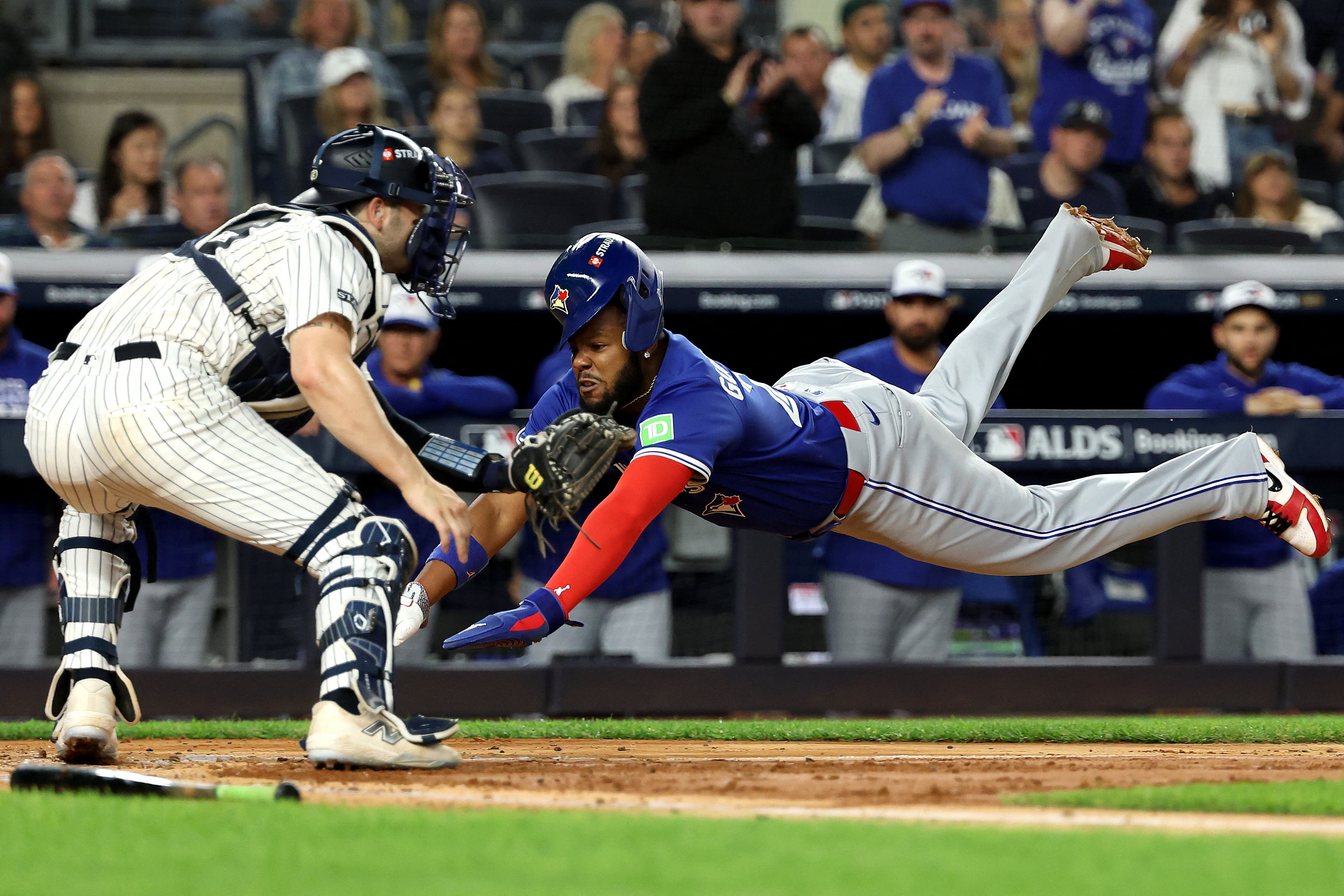 Vladimir Guerrero Jr. de los Azulejos de Toronto se lanza para anotar frente a Austin Wells de los Yanquis, durante el partido por la serie de División de la Liga Americana.