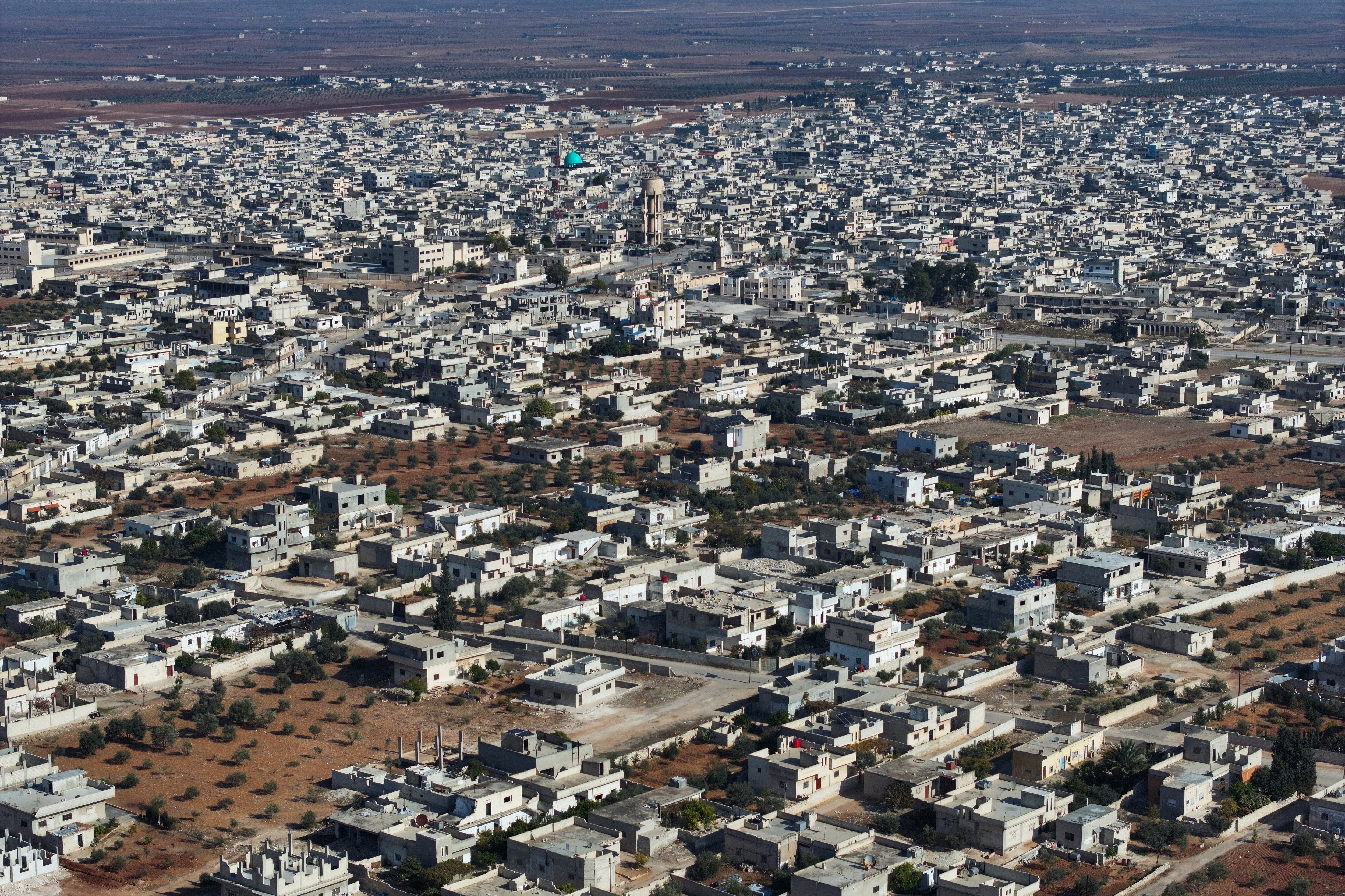 Vista aérea de una ciudad en Siria con edificios blancos y zonas desérticas en el fondo, reflejando los efectos del conflicto.