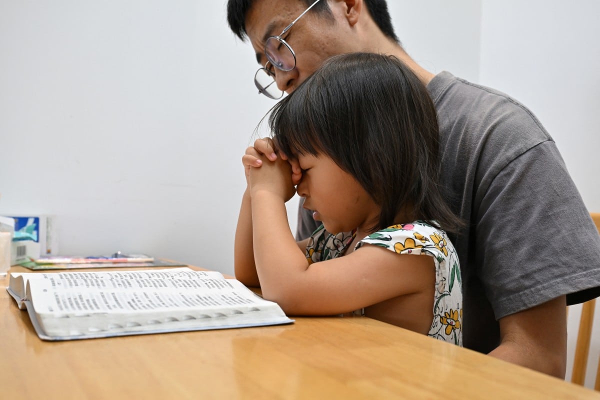 Ren Zhong, esposo de la pastora detenida Wang Cong, lee una copia de la Biblia y reza junto a su hija Huanle en su casa en Beihai, en la provincia de Guangxi, al sur de China, el 29 de julio de 2026.