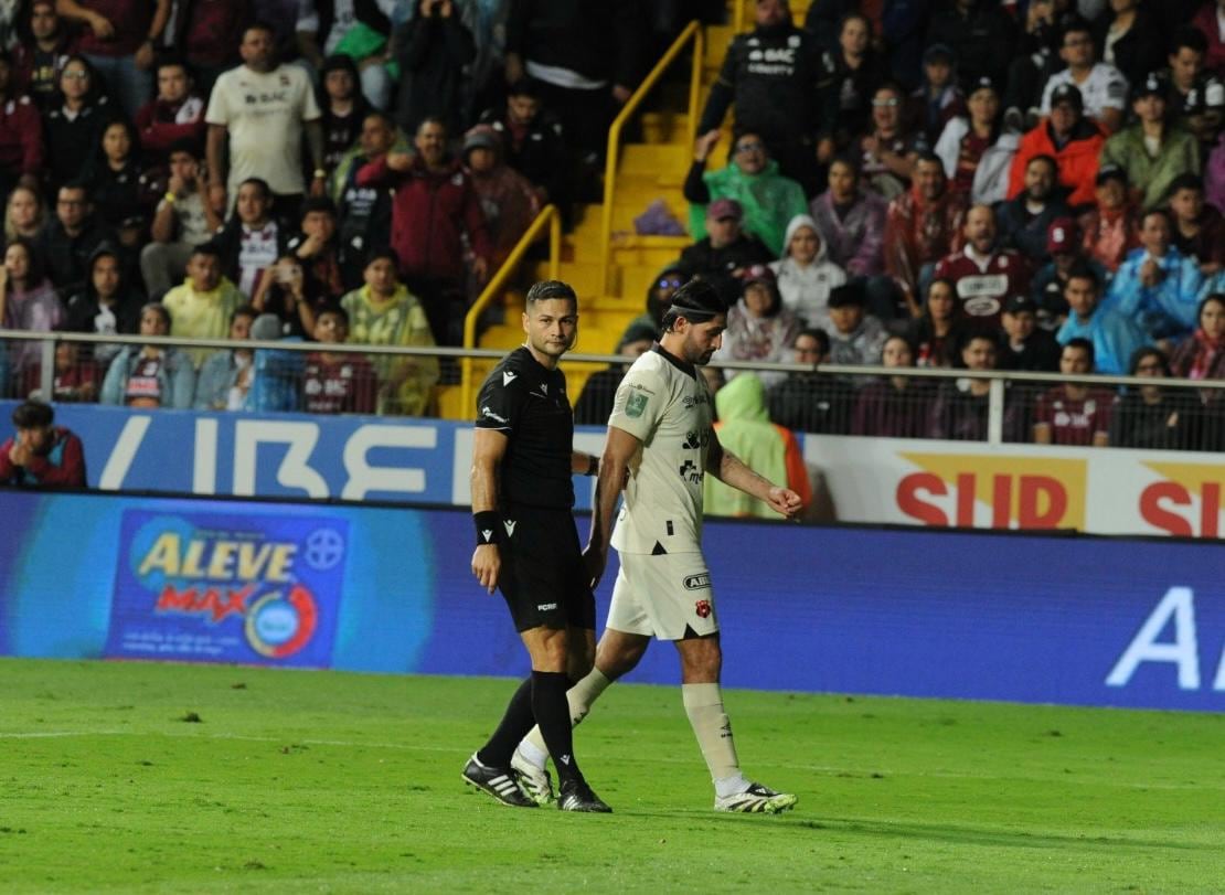 Aarón Salazar abandona la cancha tras la expulsión en el clásico Saprissa vs. Alajuelense. Observa el árbitro Keylor Herrera.