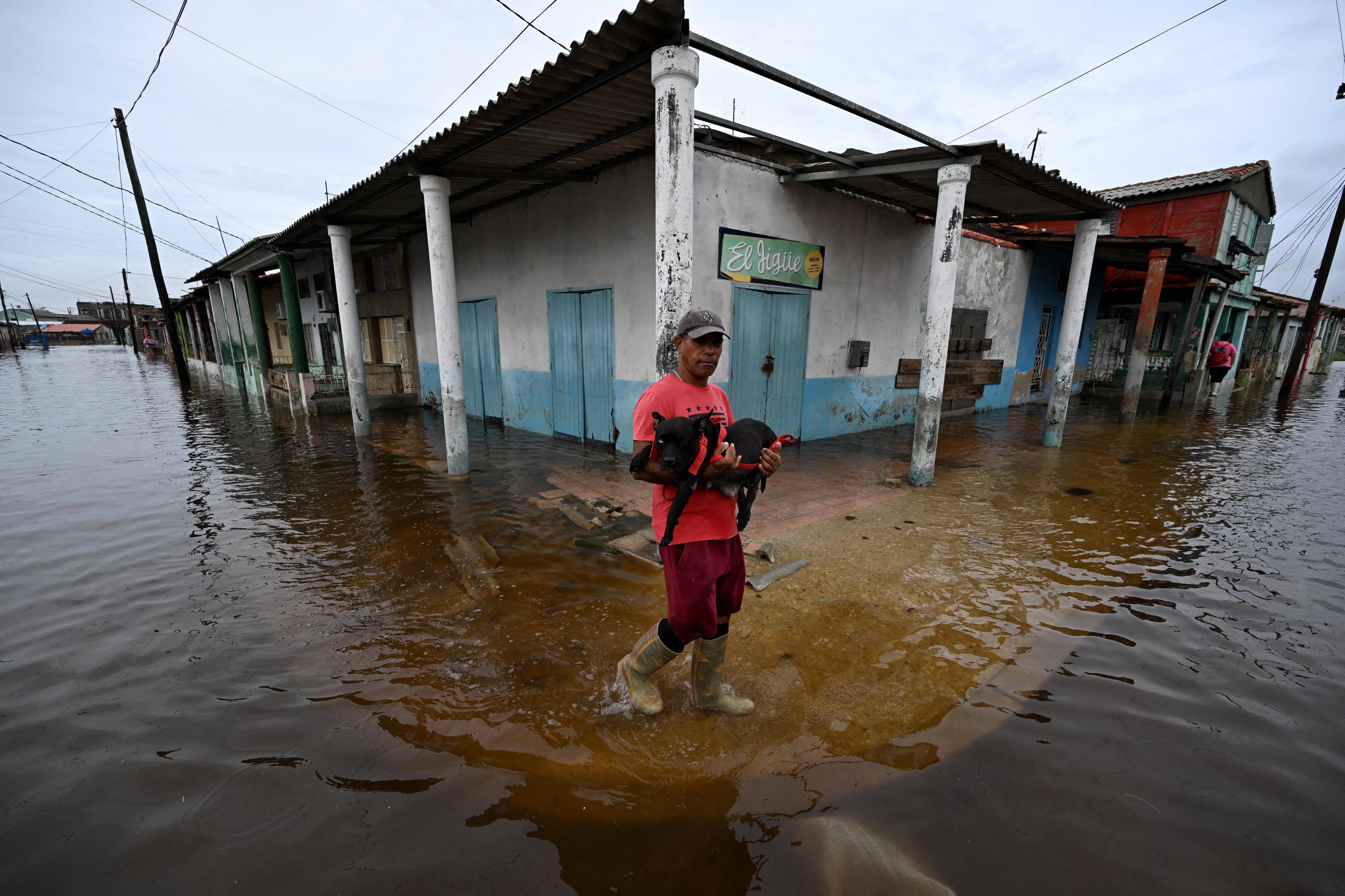 Un hombre lleva a un perro mientras camina por una calle inundada tras el paso del huracán Rafael en Batabano, provincia de Mayabeque, Cuba.