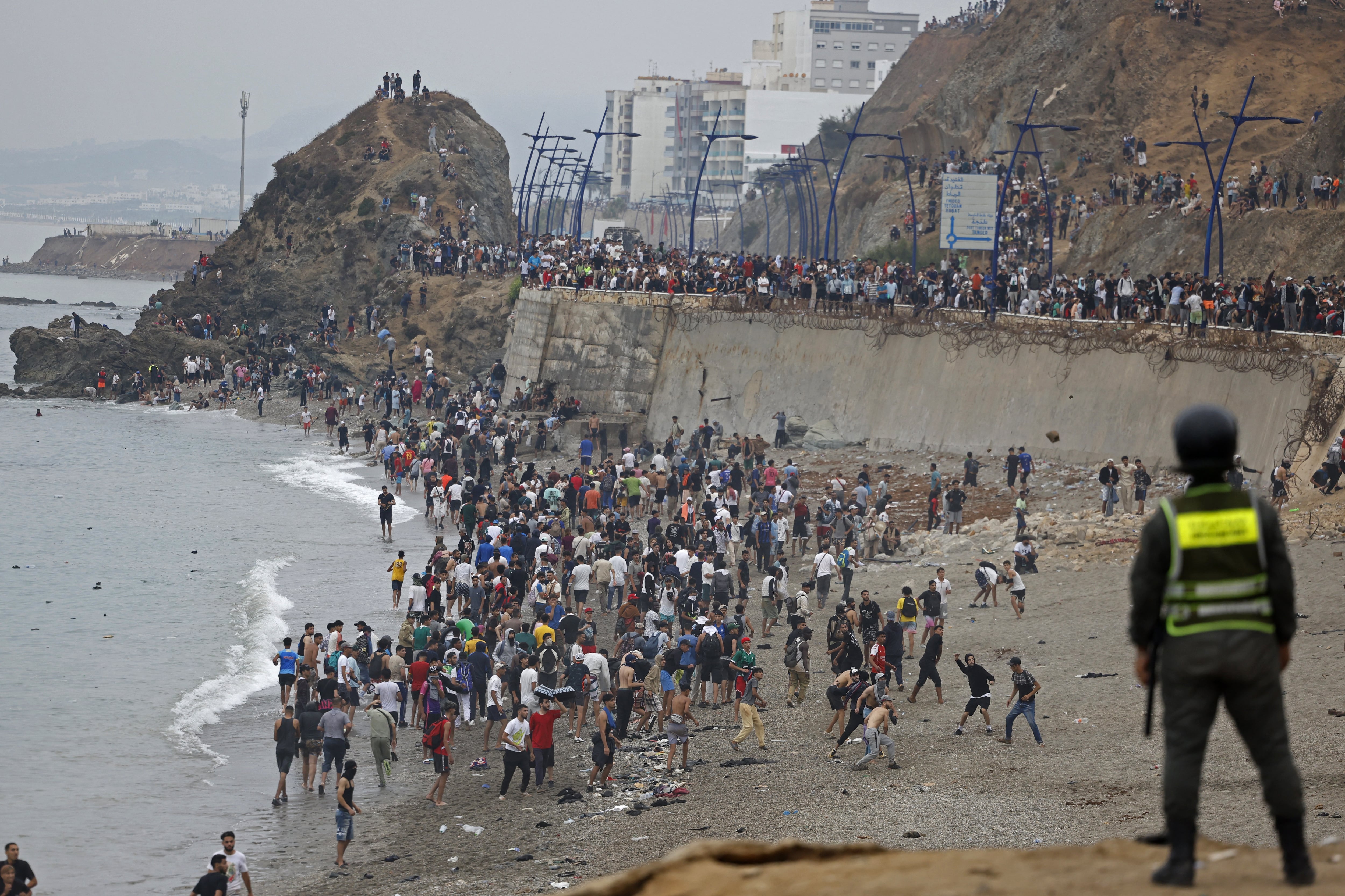 Migrants gather along the fence at the site of clashes near Fnideq, on the Morocco-Spain border, on July 31, 2026. Thousands of migrants crossed overnight from Morocco into Spain's north Africa's Ceuta enclave, a police source said on July 31, adding that it was impossible to estimate how many people in total. A total of 18 people died while attempting to reach the Spanish enclave, the source said. (Photo by Abdel Majid BZIOUAT / AFP)