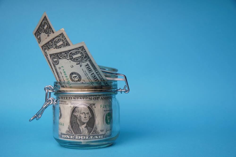 Un frasco de vidrio con billetes de dólar sobre un fondo azul, representando ahorro en dólares, en el contexto de la dolarización de los depósitos bancarios en Costa Rica.