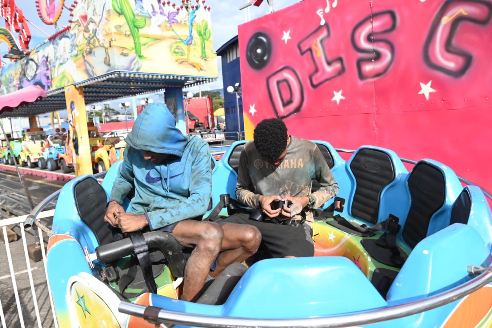 Dos trabajadores en un juego mecánico se cercioran de que los cinturones de seguridad estén bien puestos.