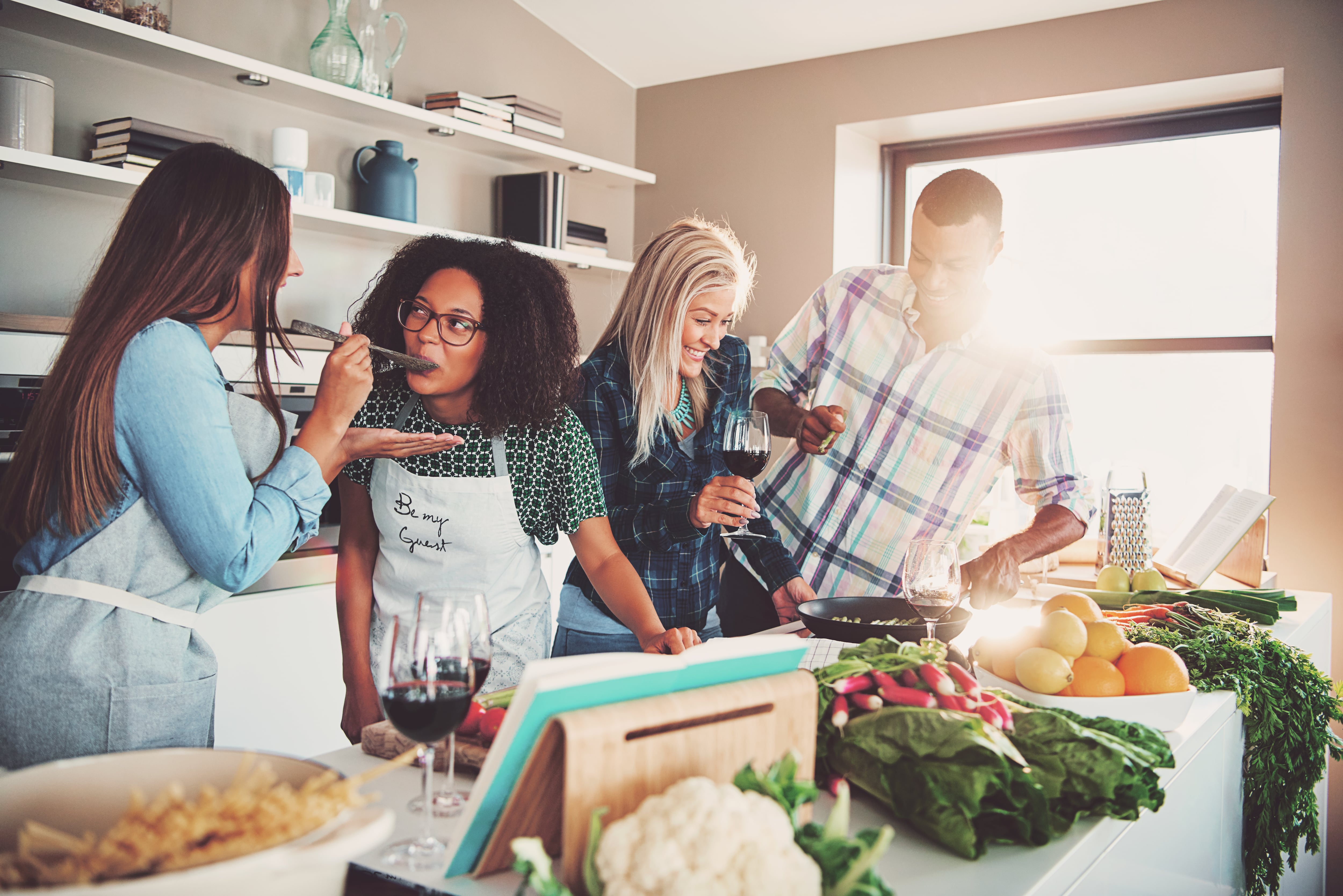 Jovial grupo de amigos en una cocina, preparando juntos una receta, probando comida, preparación de alimentos, cocinar