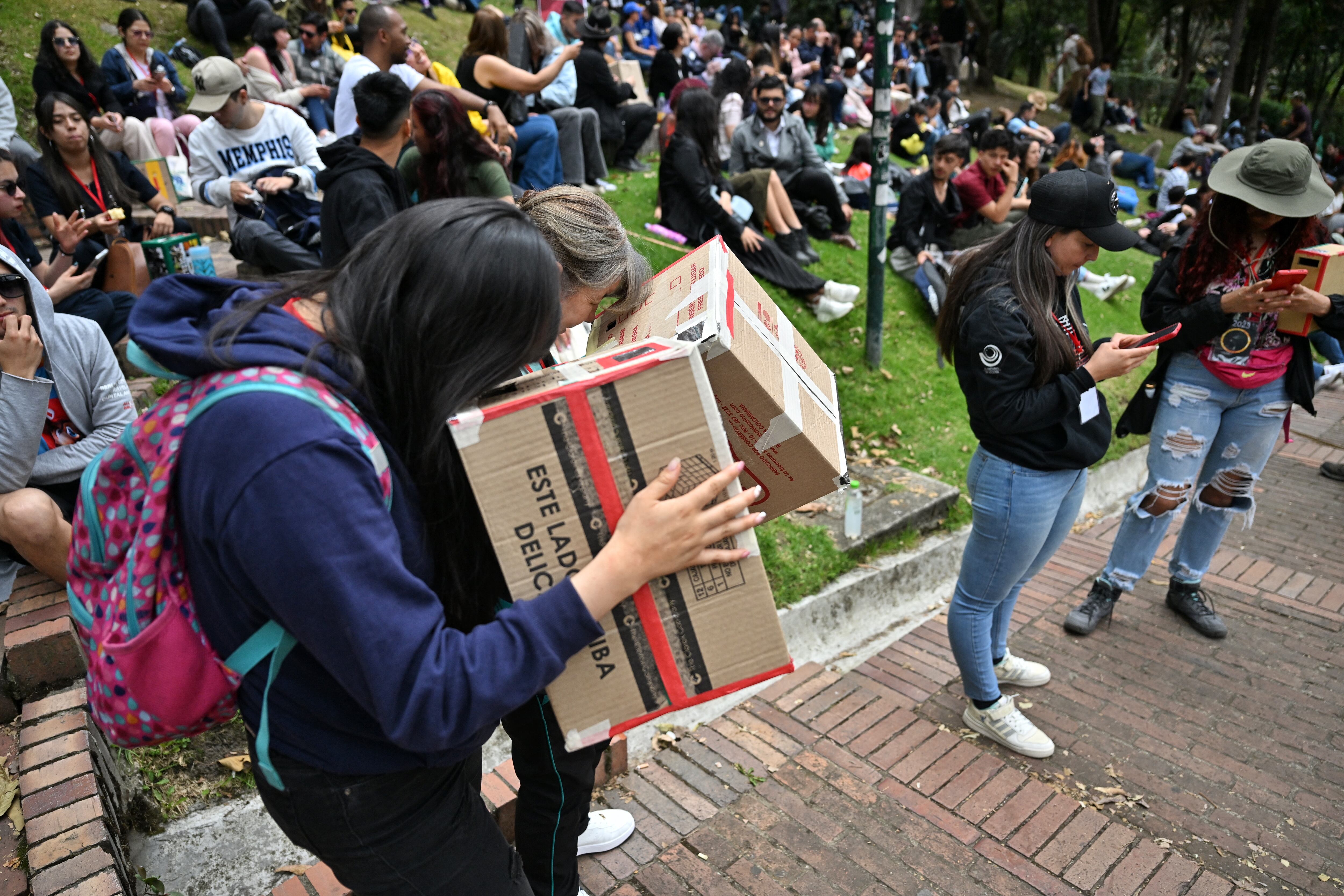 Mujeres utilizan proyectores estenopeicos para observar el eclipse solar anular en Bogotá, Colombia.