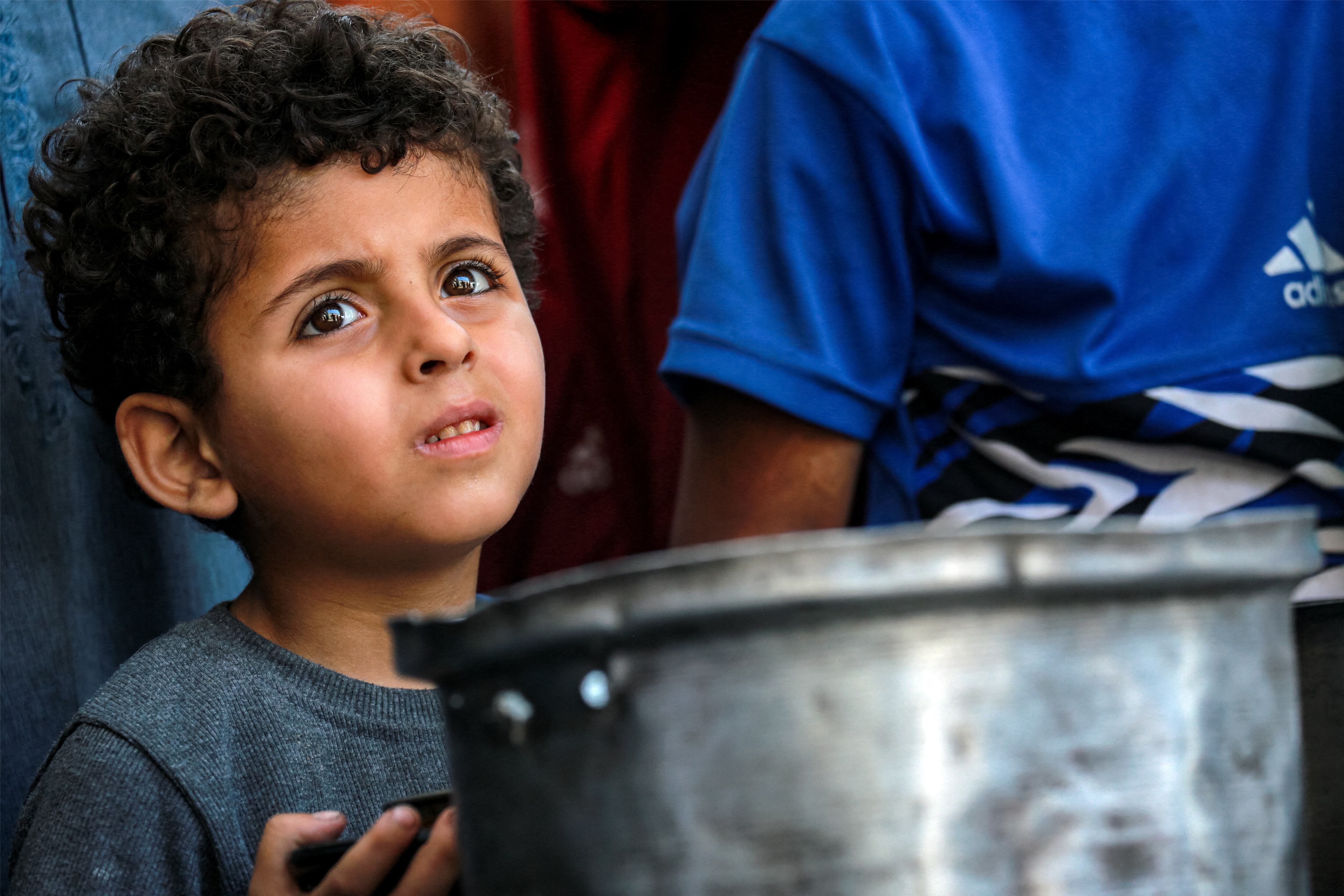 Un niño observa mientras espera a la gente que hace fila con ollas para recibir comida de un comedor social en la ciudad de Gaza, el 14 de julio de 2025. (Foto de Bashar TALEB / AFP)