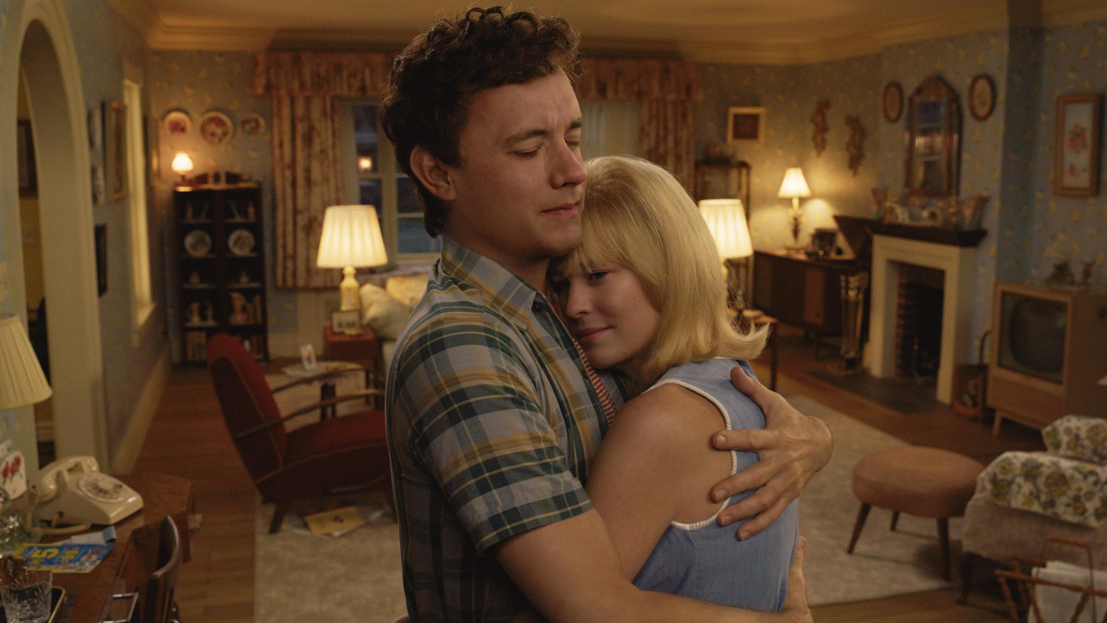 Escena de la película 'Here', en la que Tom Hanks abraza a Robin Wright en la sala de una casa. Ambos lucen varias décadas menores.