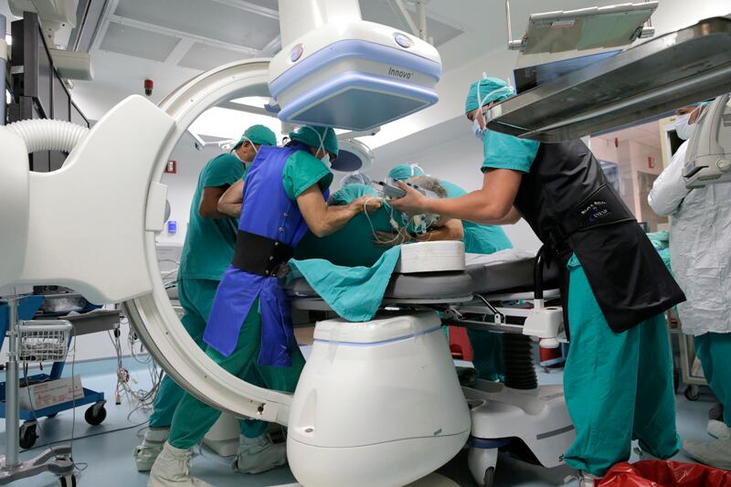 Médicos vestidos con traje verde realizan procedimiento con un equipo conocido como arco en C por su forma. Están en un quirófano.