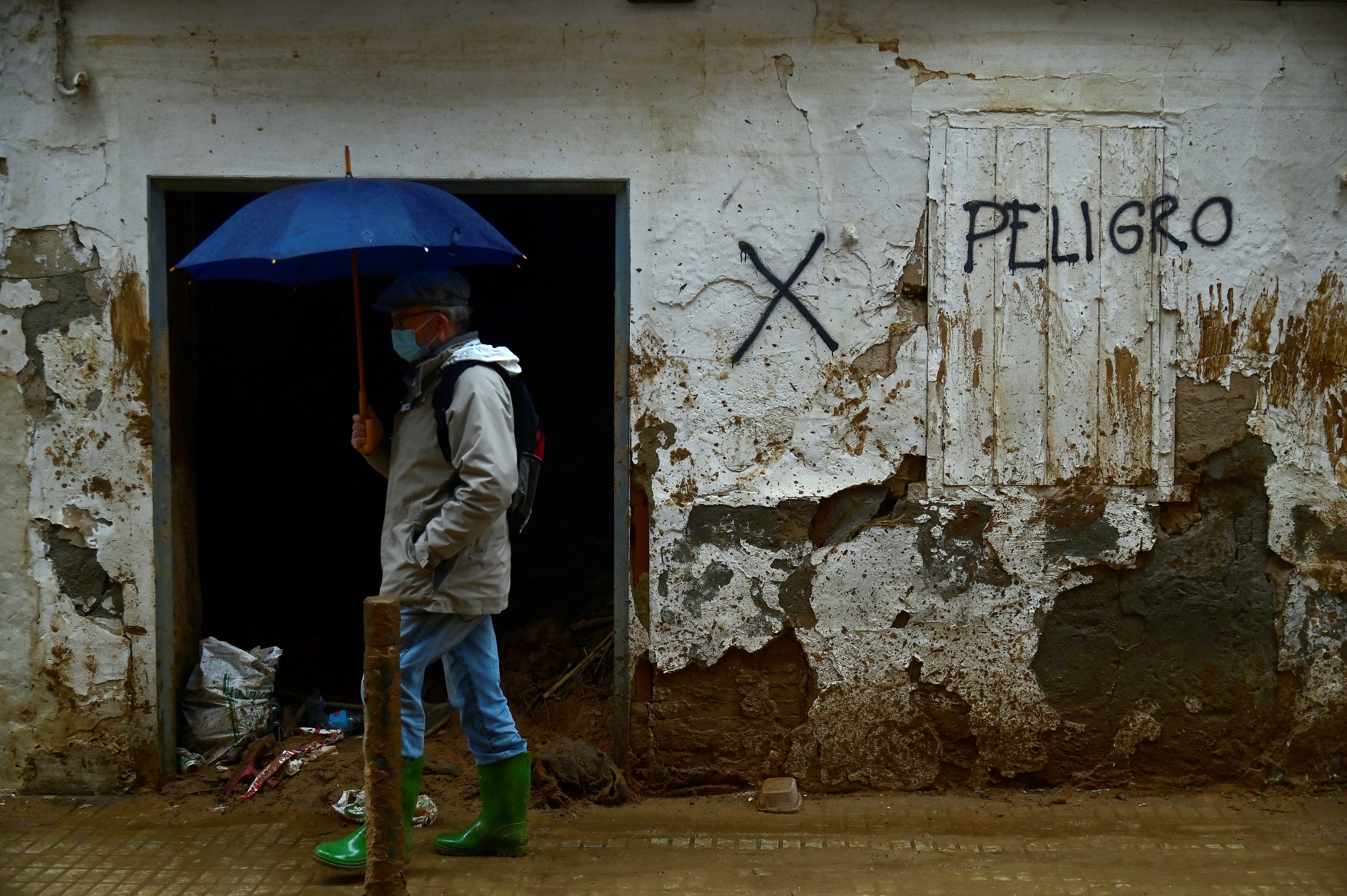 Un peatón se protege de la lluvia bajo un paraguas mientras camina cerca de un escrito que dice 'Peligro' en una calle de Paiporta, al sur de Valencia, este de España.