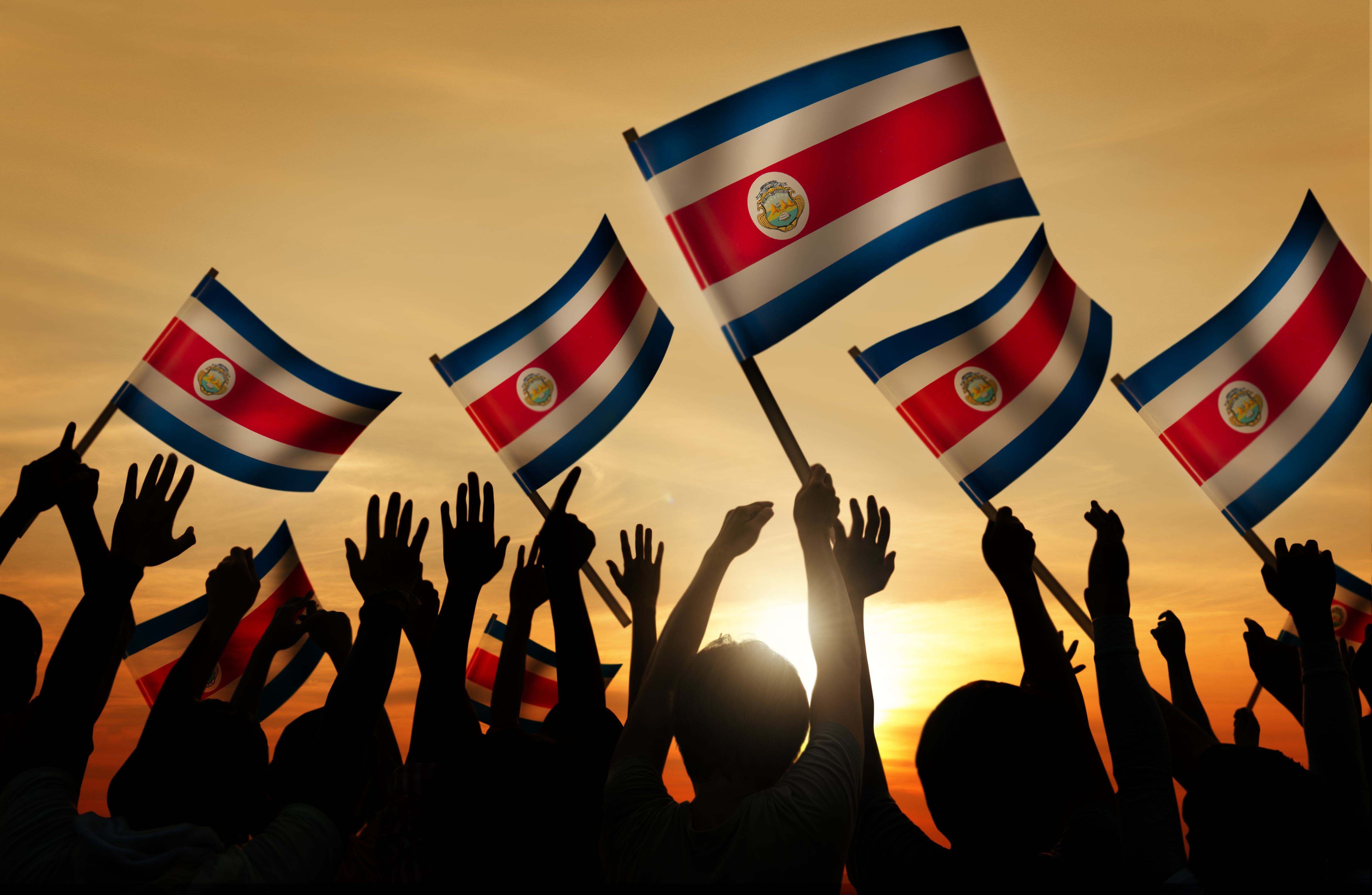 Multitud de niños a contraluz sosteniendo banderas de Costa Rica al atardecer