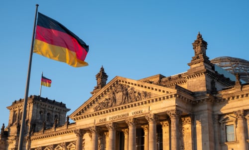 Vista del edificio del Reichstag, sede del Parlamento alemán, con la bandera de Alemania ondeando al atardecer.