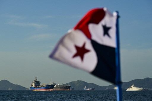 Bandera de Panamá en primer plano con buques navegando cerca del canal de Panamá.